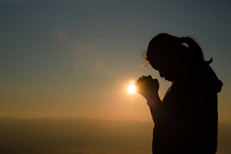 Adolescente rezando com o sol nascendo