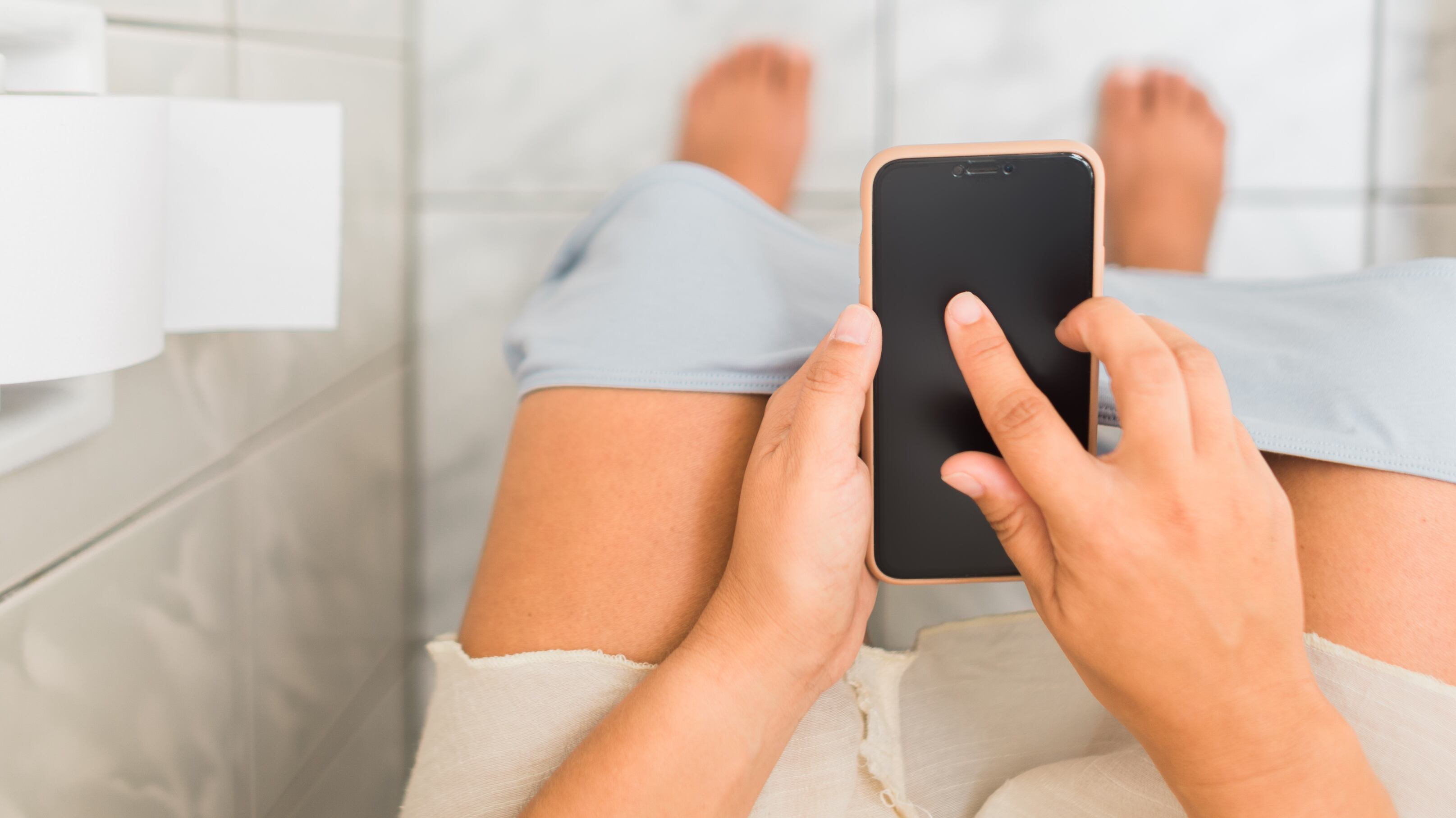 Imagen referencial de una persona con un dispositivo celular en el baño.