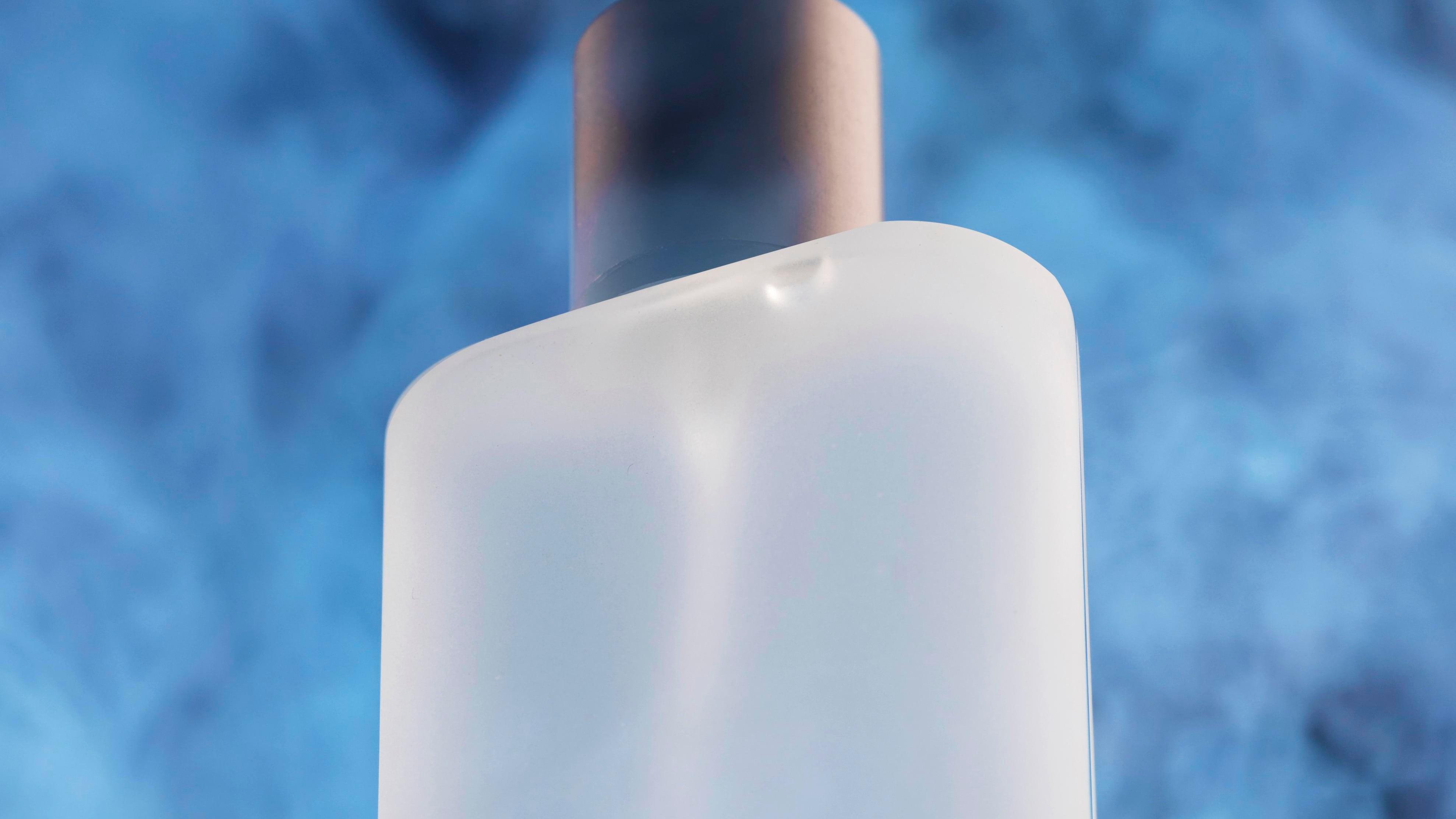 Frasco de perfume branco com tampa prata e fundo azul