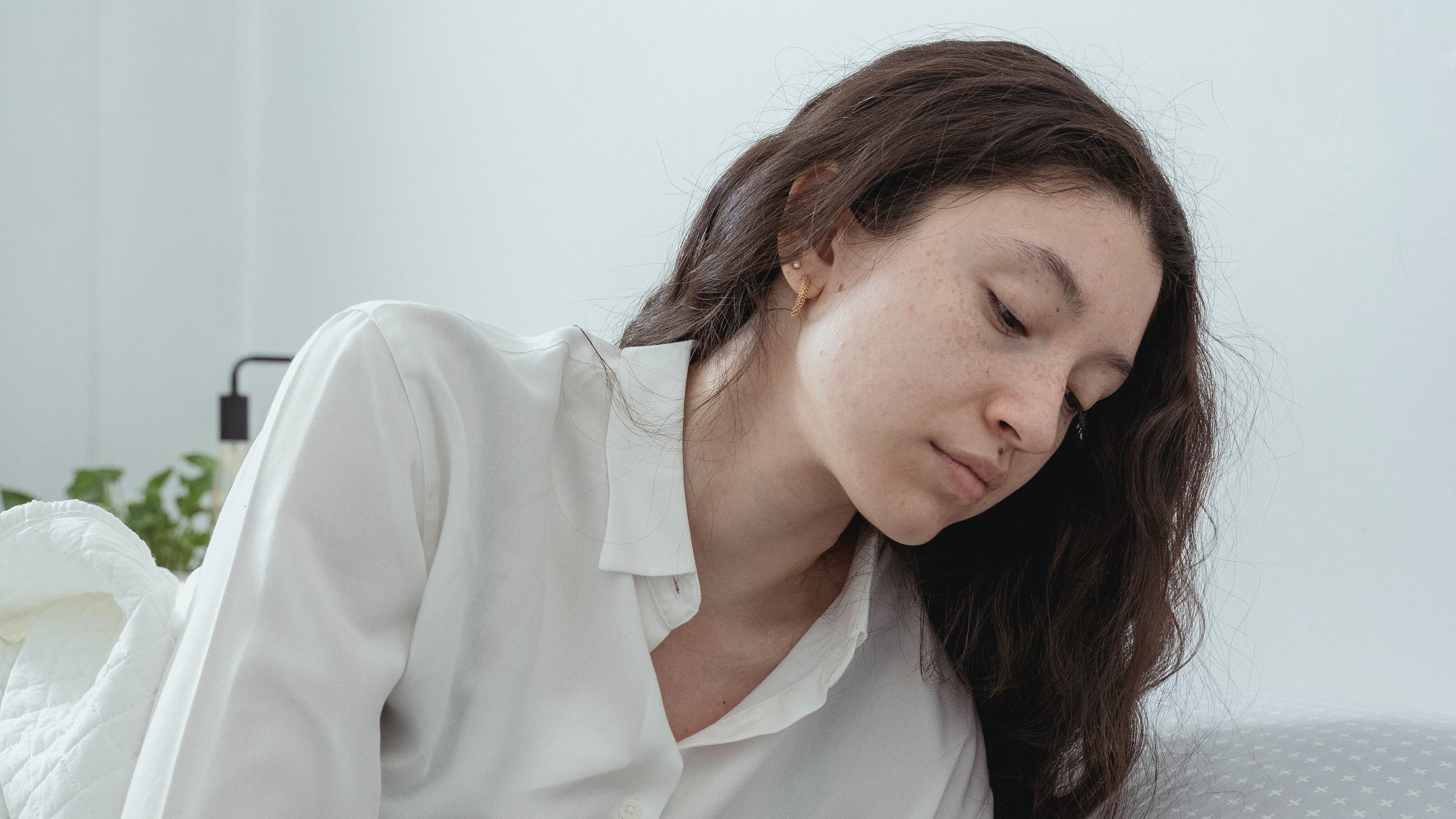 Mulher deitada com pijama branco segurando celular na cabeceira da cama