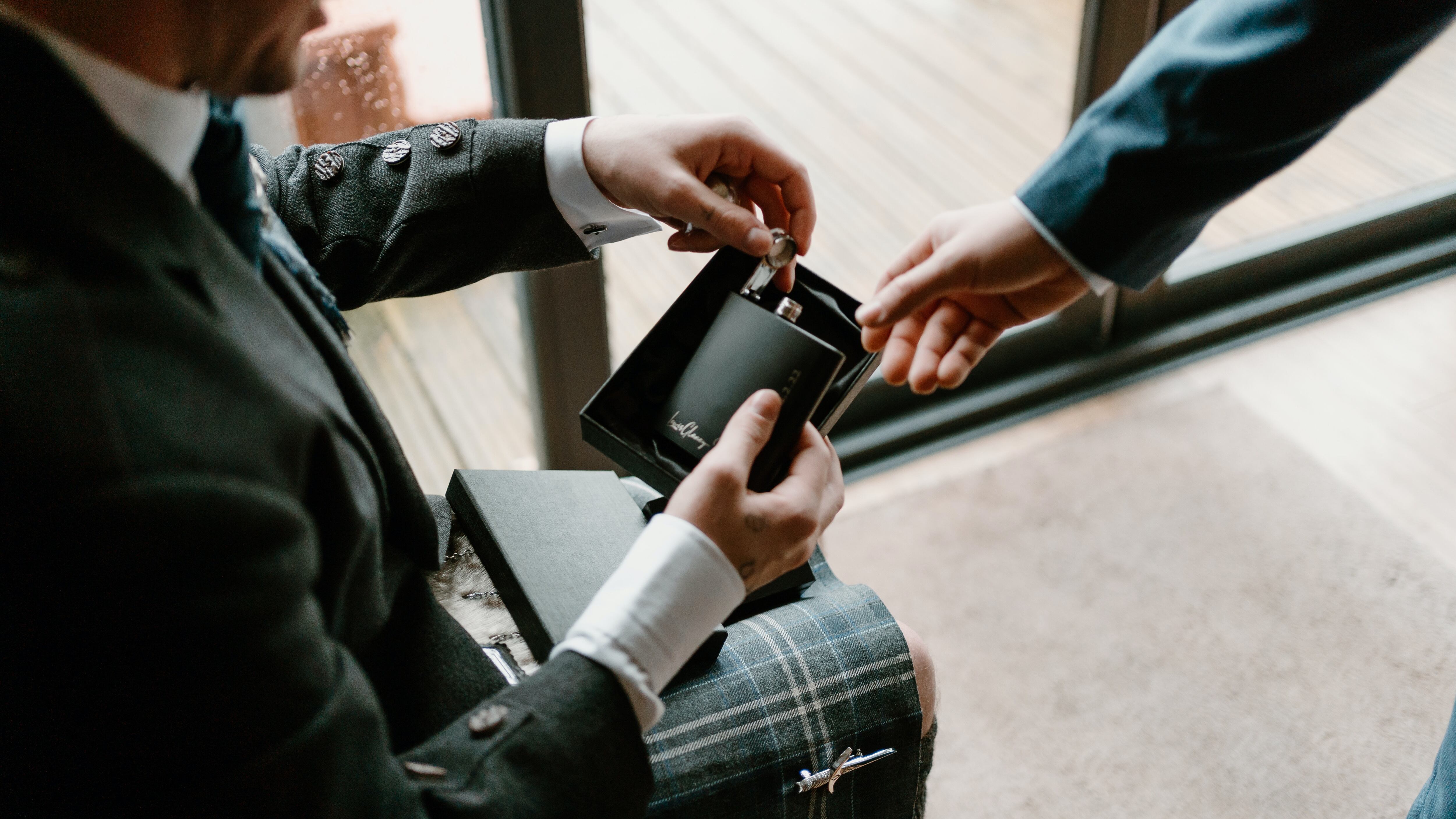 Homem de terno e saia escocesa segurando frasco de perfume