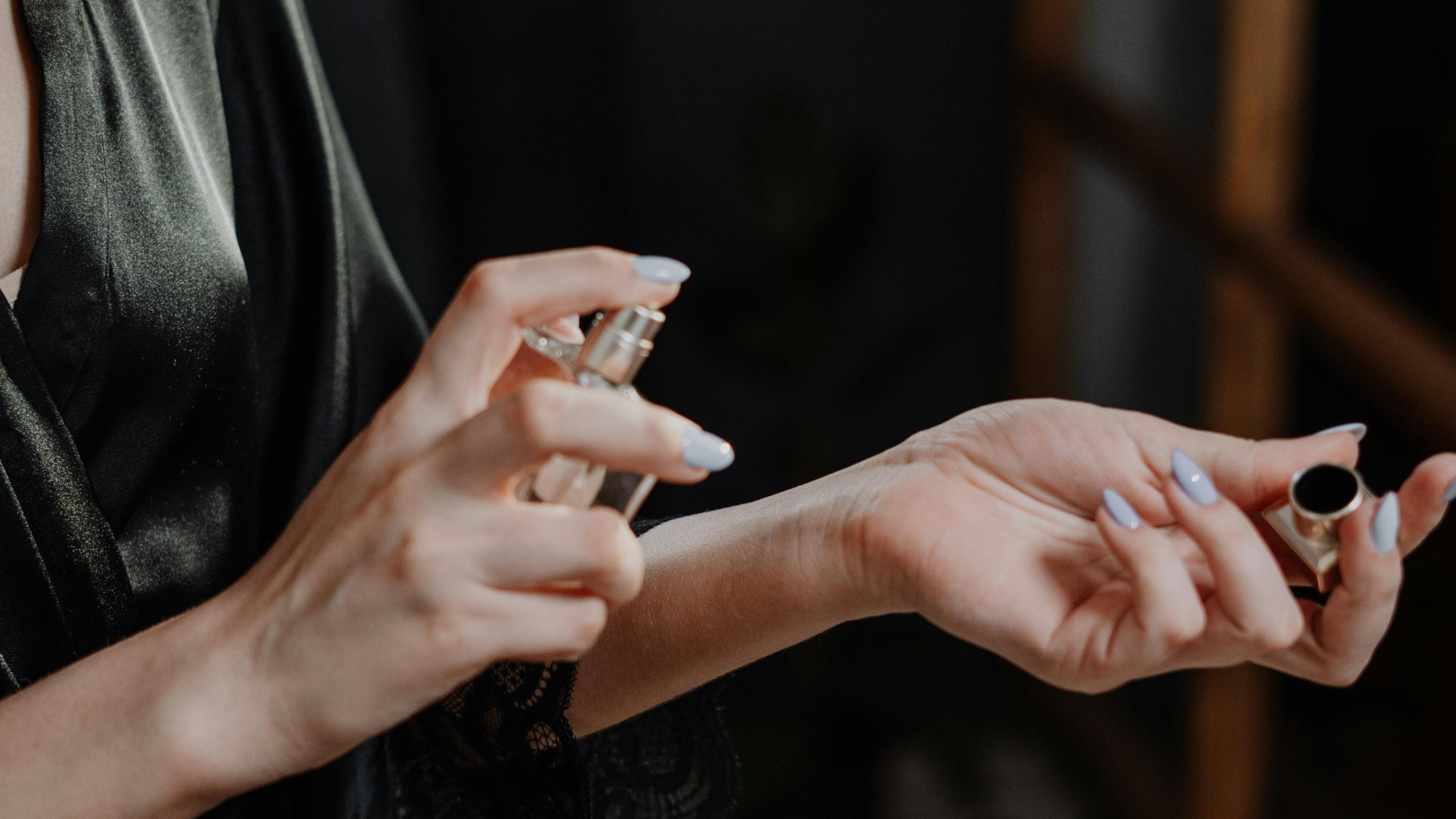 Mulher com roupão de seda preto borrifando perfume no pulso