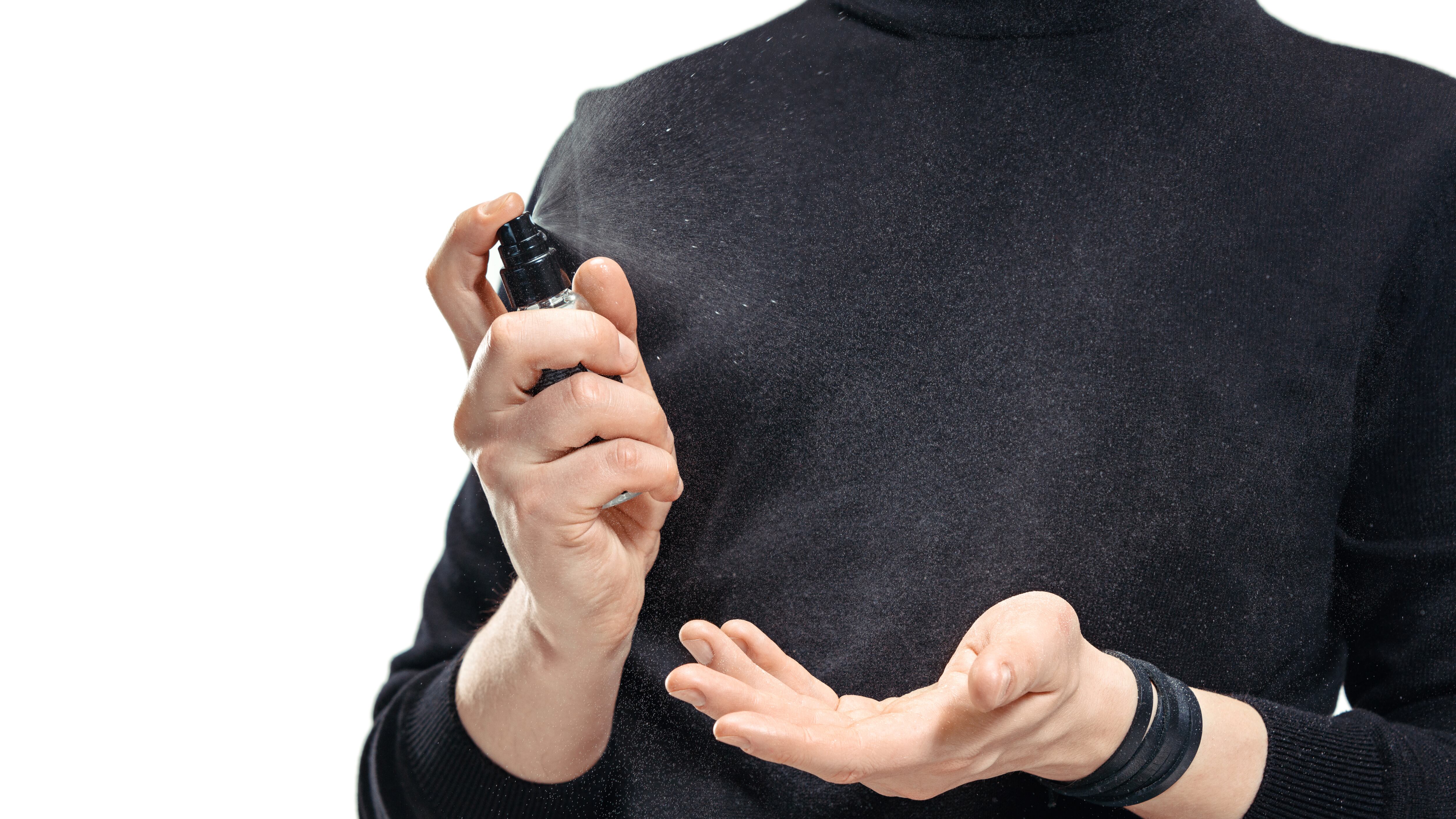 Homem de preto borrifando perfume