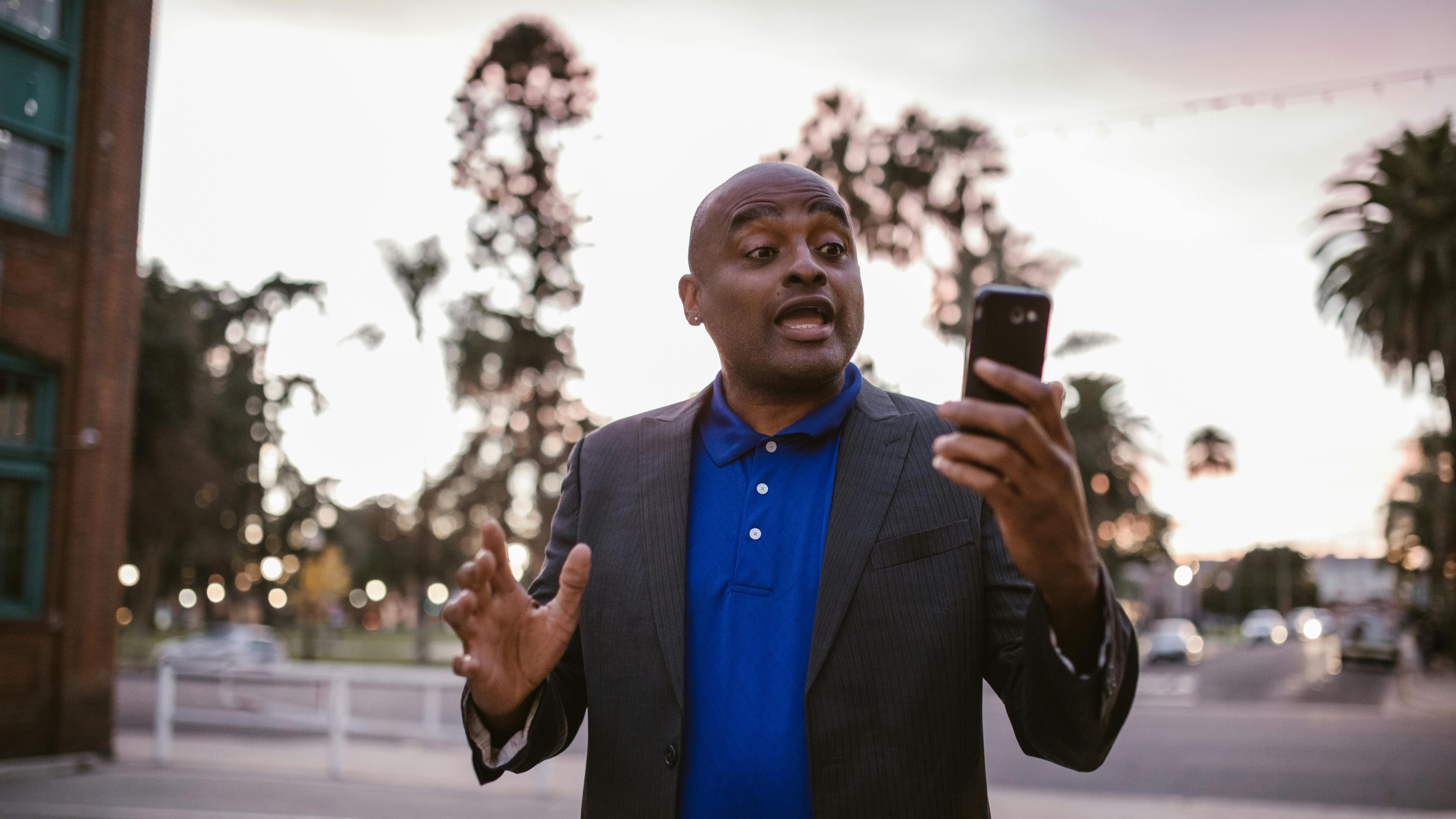 Homem negro careca de terno olhando para o celular na rua