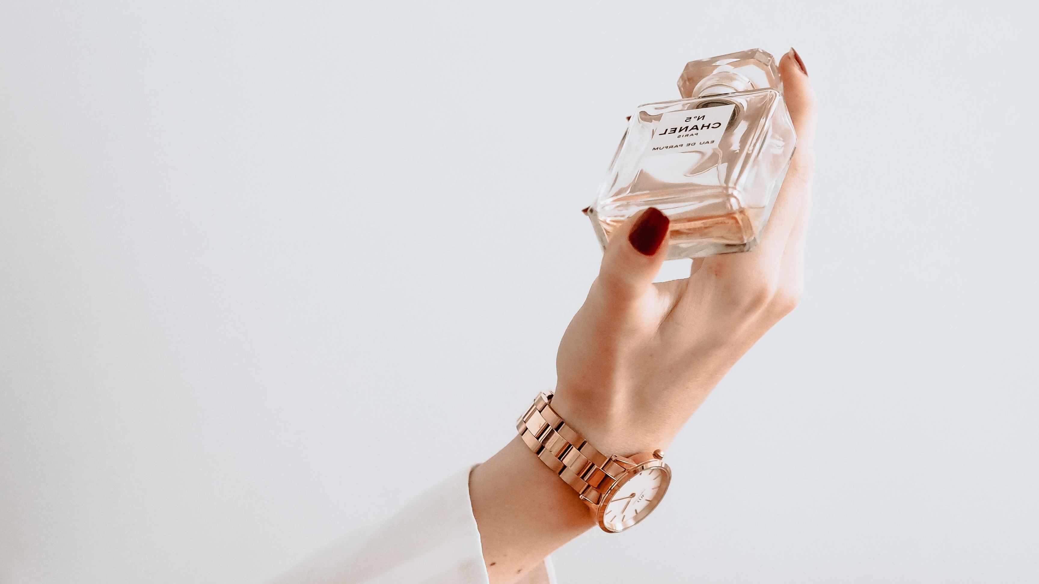 Silhueta de braço feminino com relógio segurando frasco de perfume