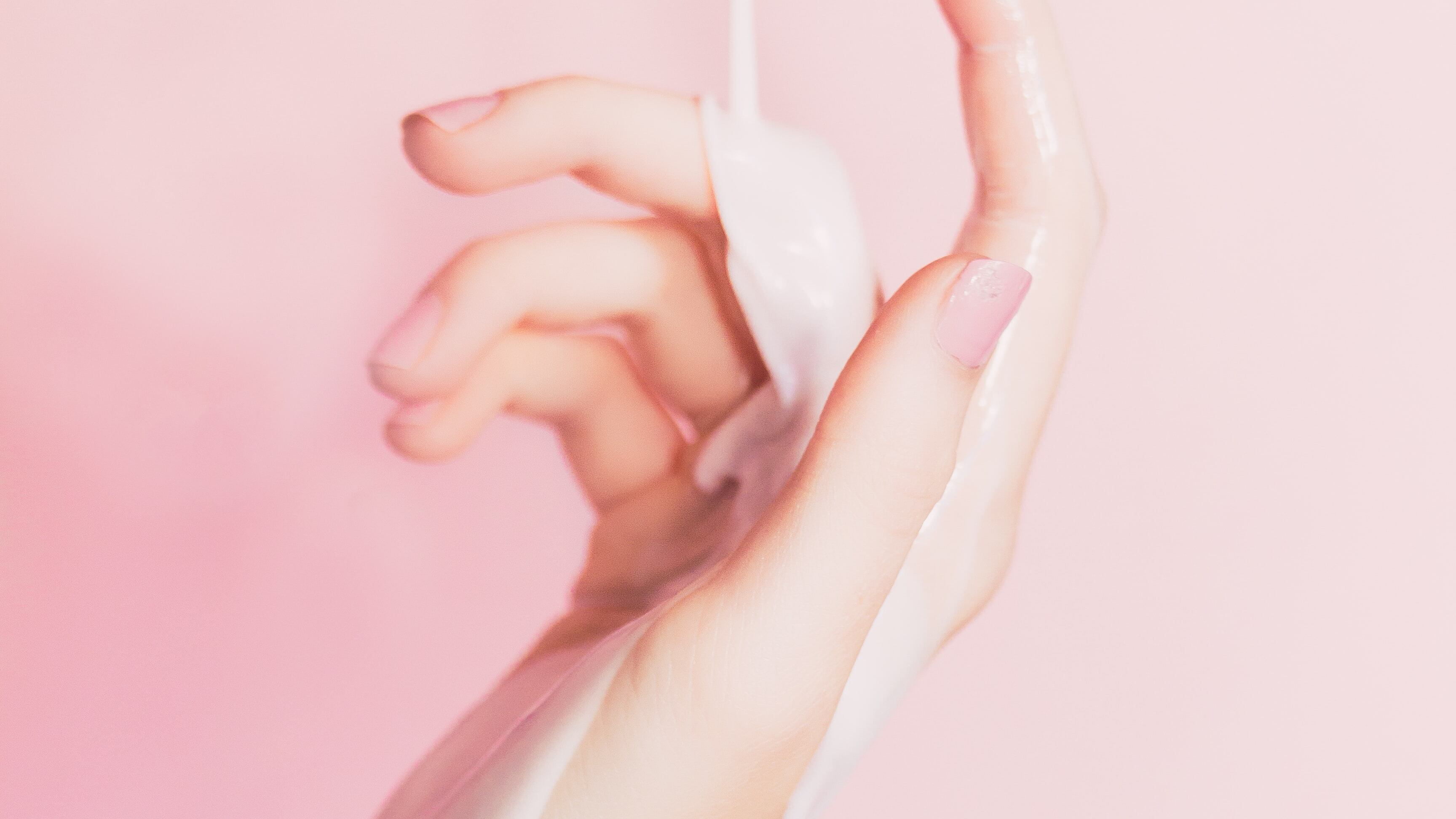 Hidratante escorrendo em mão feminina branca com fundo rosa