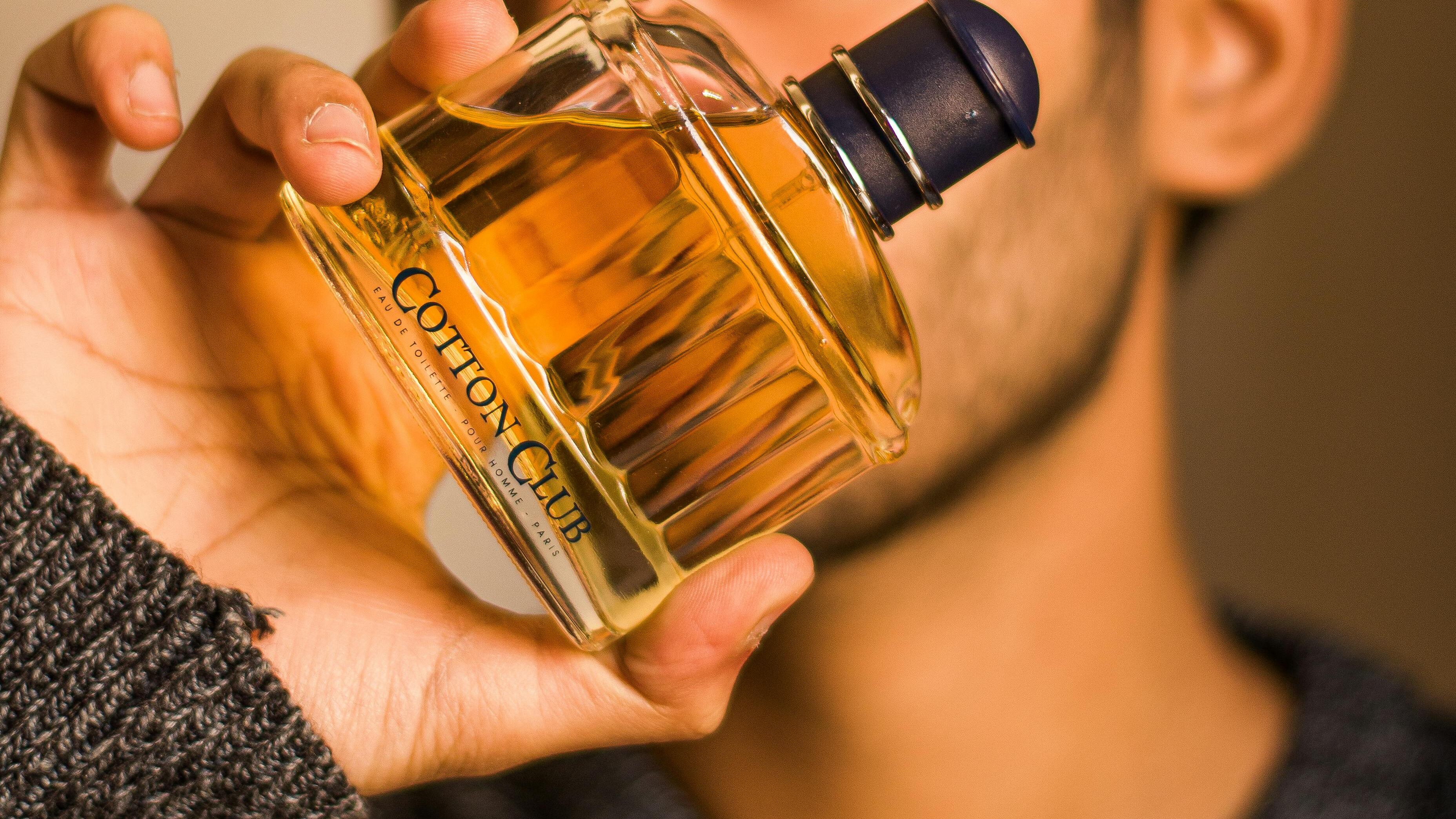 Homem segurando frasco de perfume em frente ao rosto