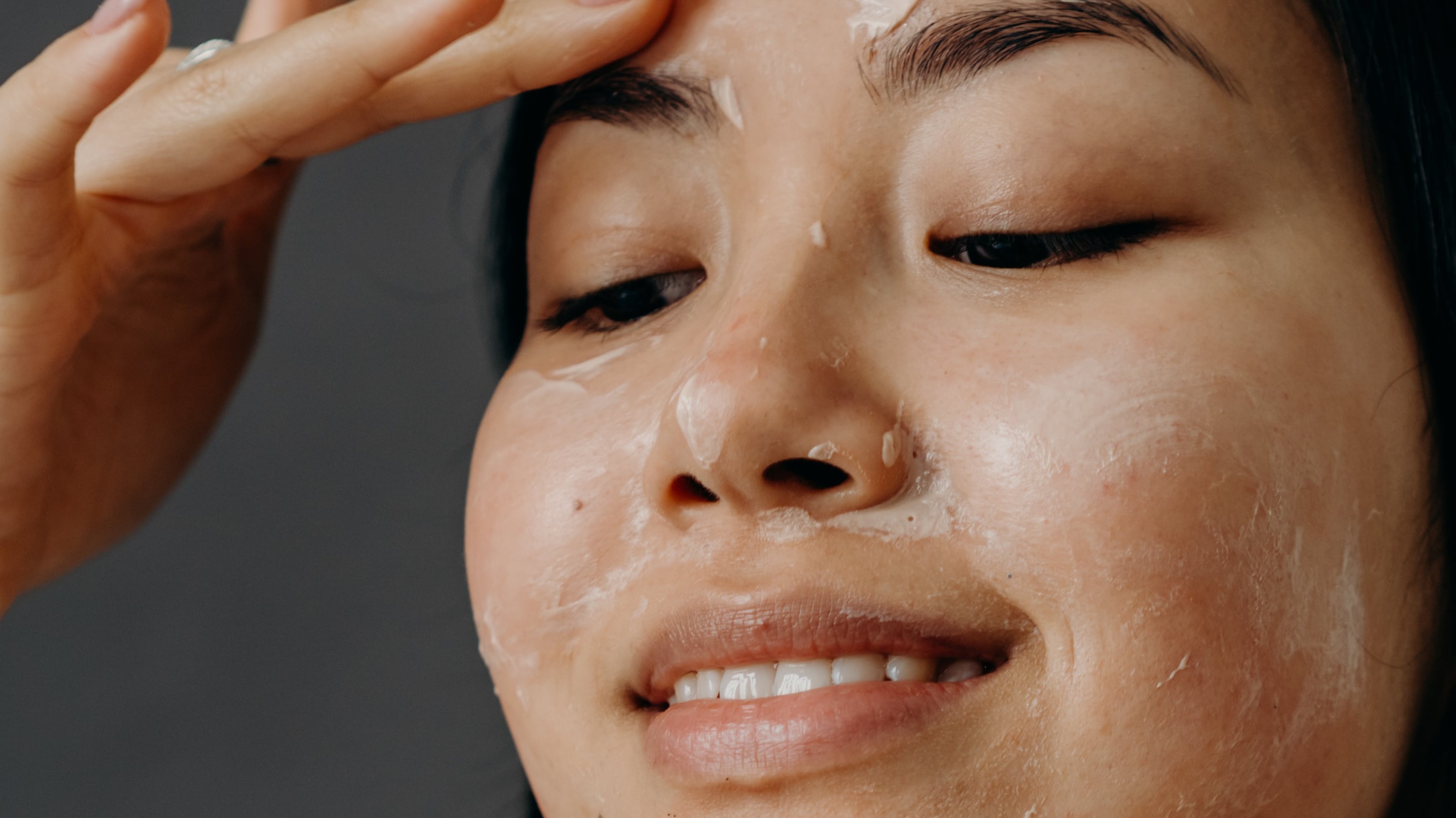 Mulher asiática sorrindo passando creme facial