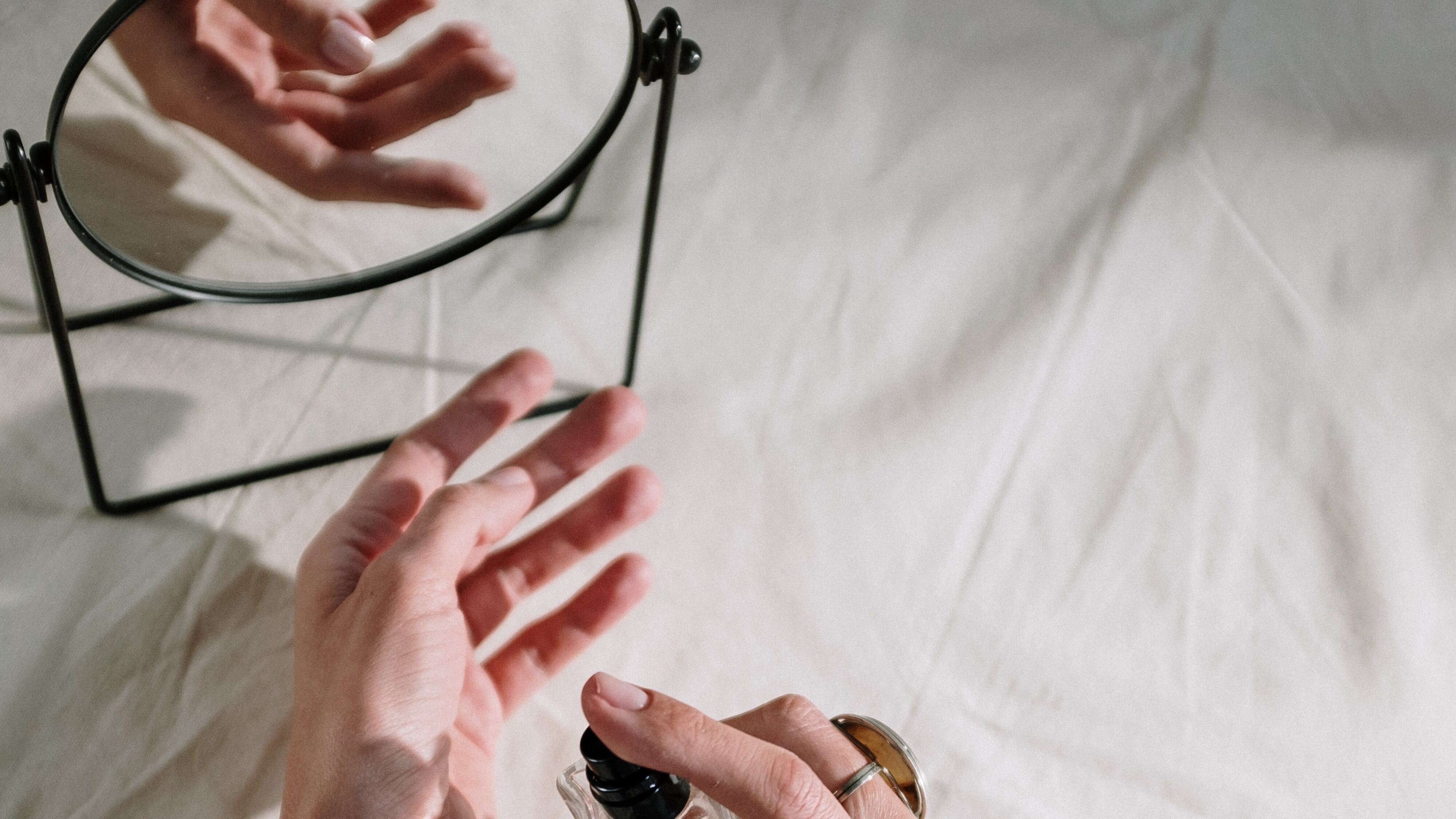 Silhuetas de mãos femininas borrifando perfume no pulso em frente ao espelho