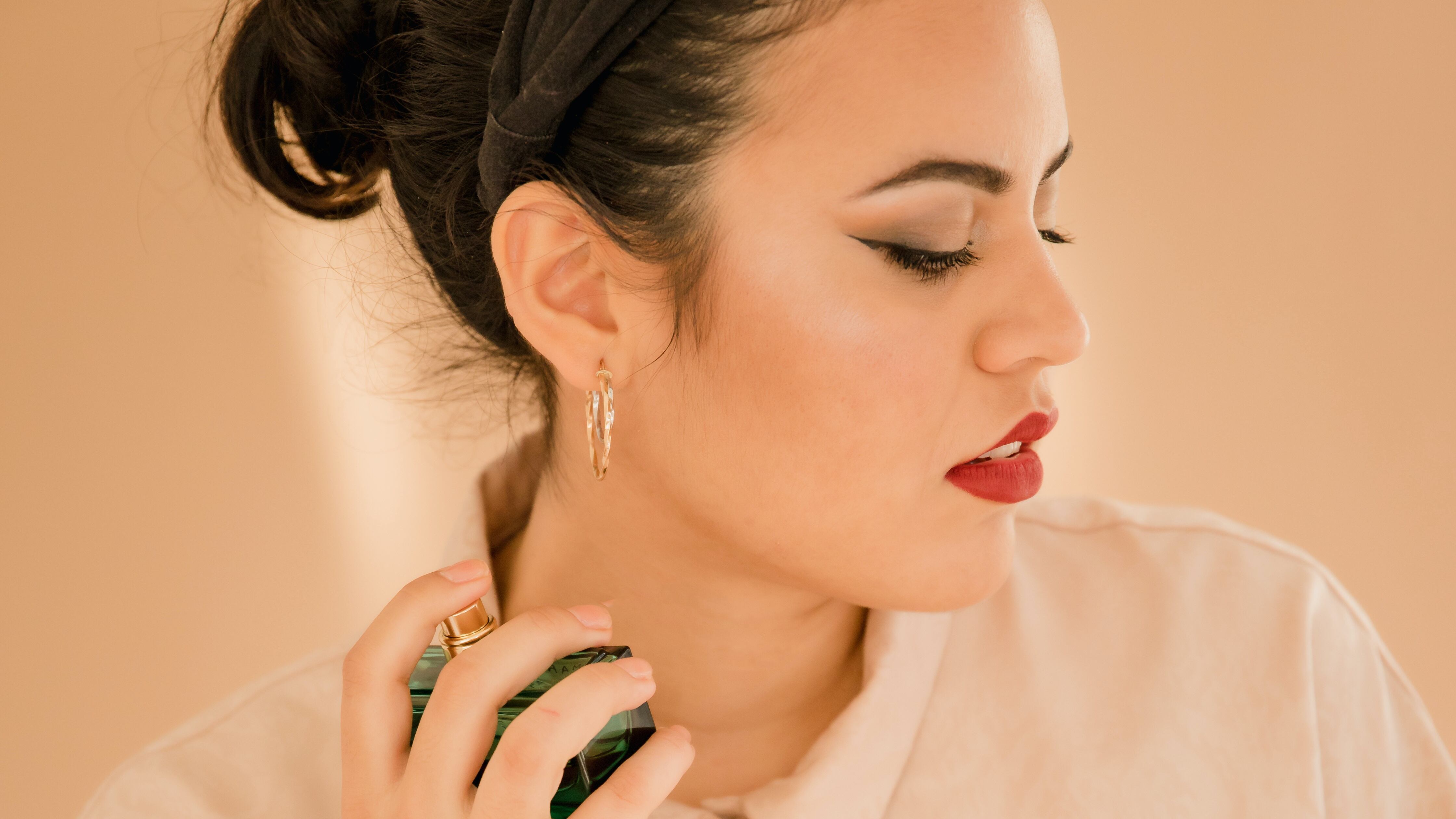 Mulher com batom vermelho aplicando perfume no pescoço