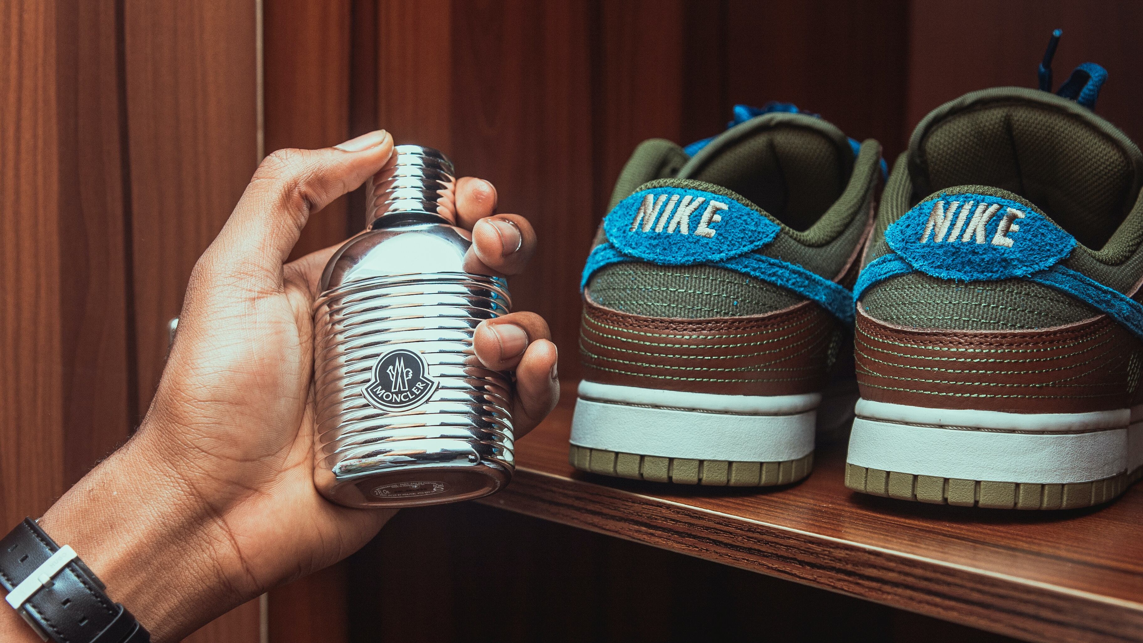 Mãos masculinas com relógio segurando frasco de perfume ao lado de tênis da Nike