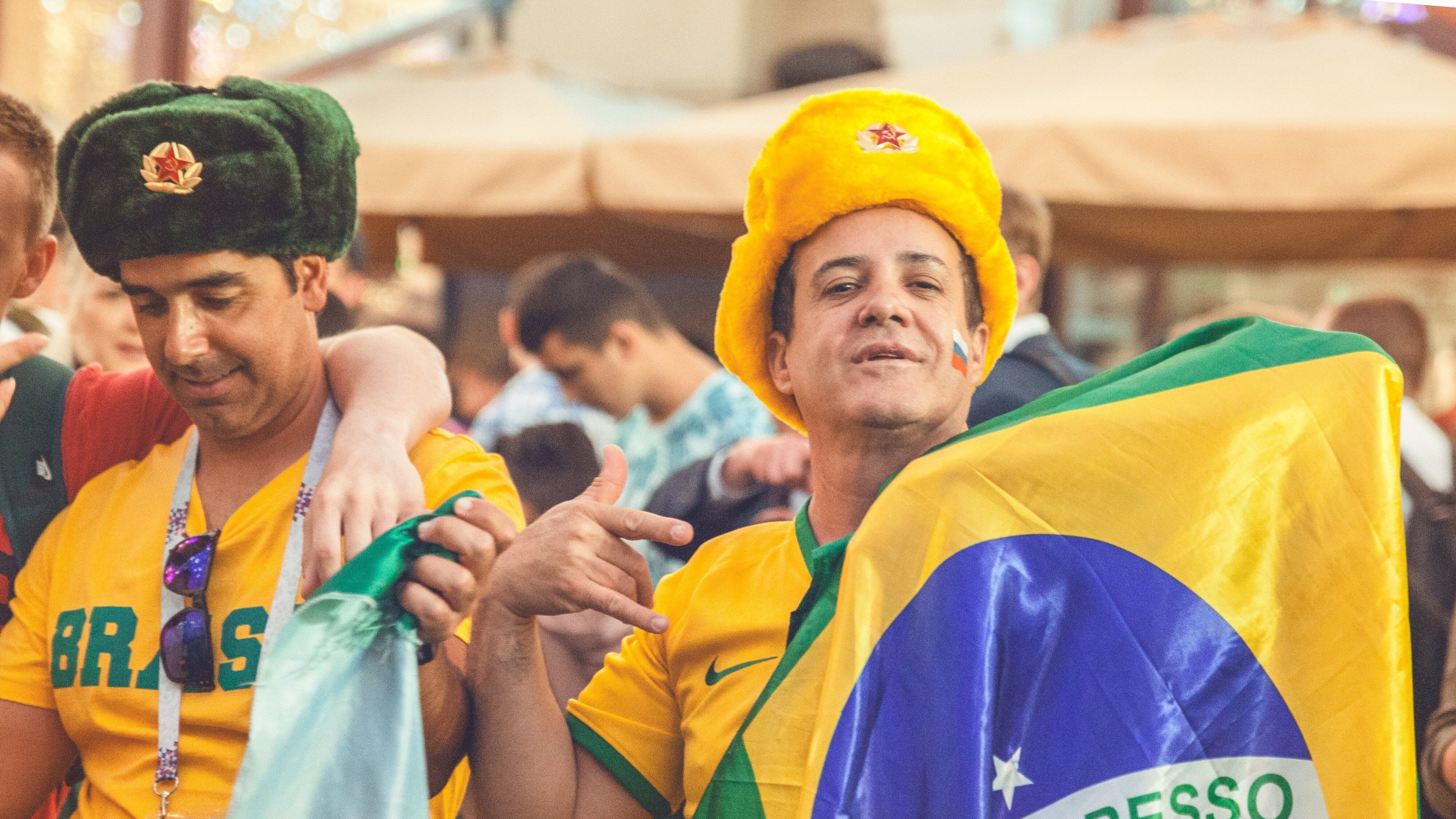 Dois homens de chapéu com camisa do Brasil segurando a bandeira do país