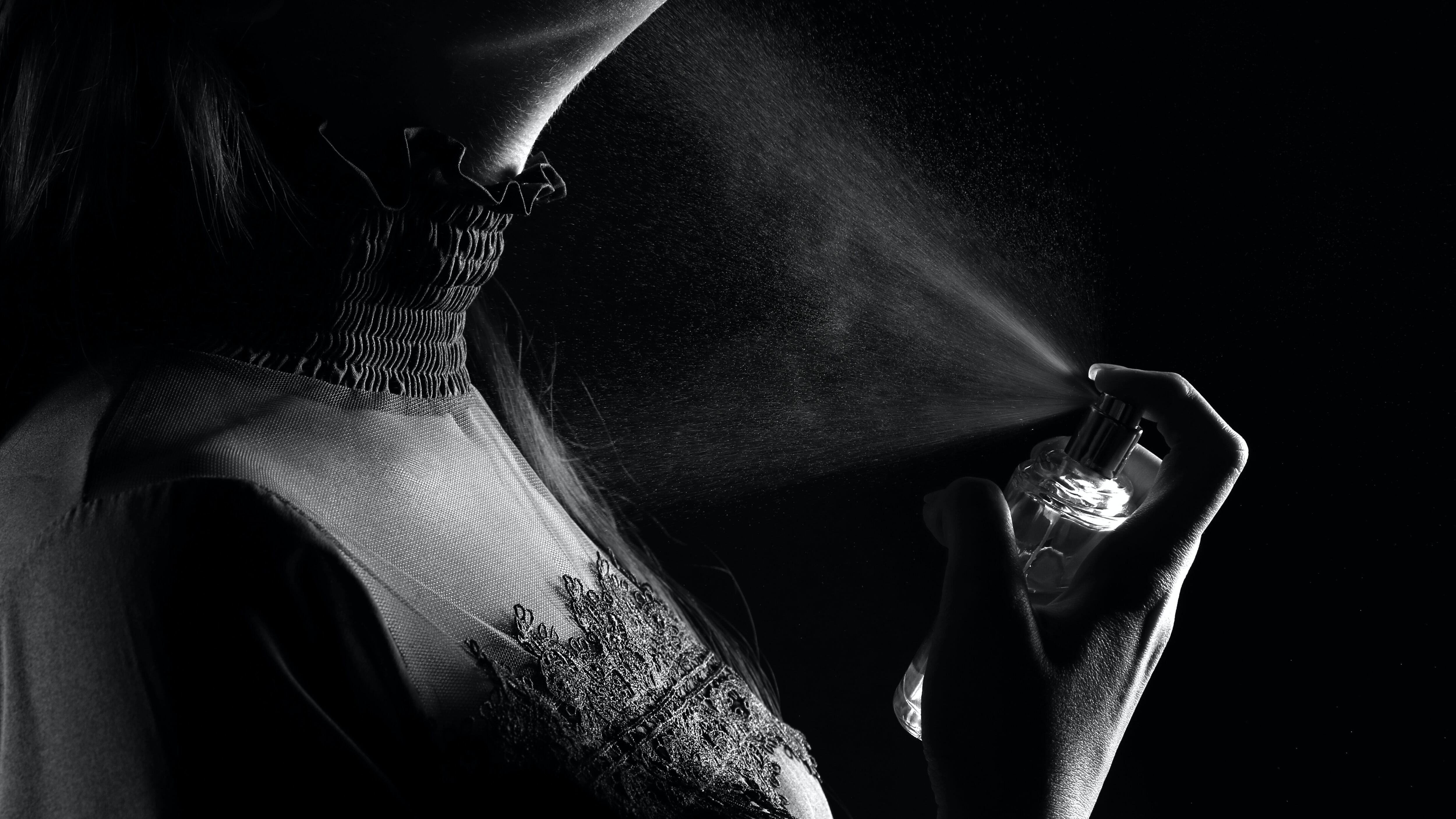 Imagem em preto e branco de silhueta feminina borrifando perfume no pescoço