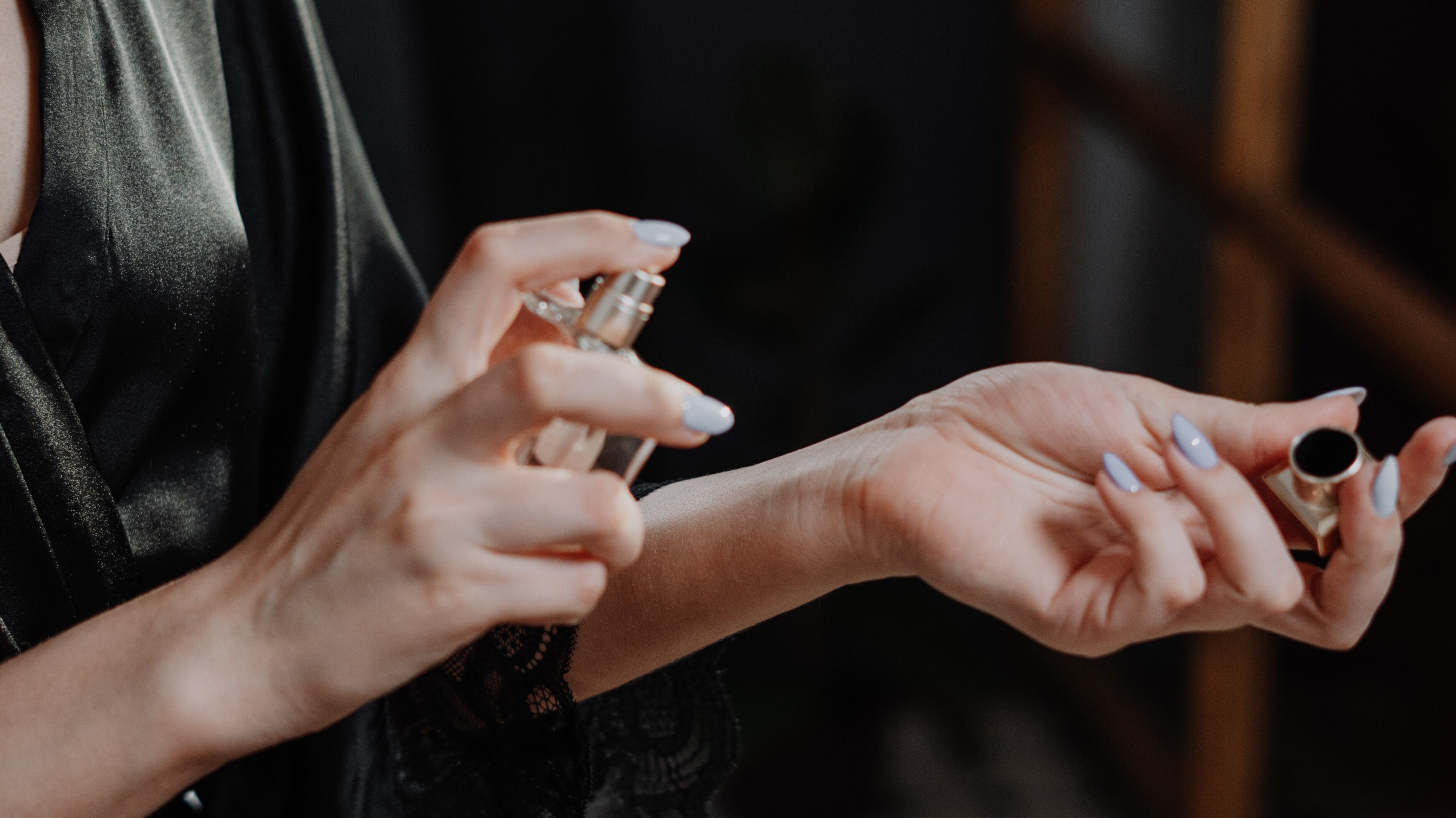 Mulher com roupão de cetim preto espirrando perfume no pulso