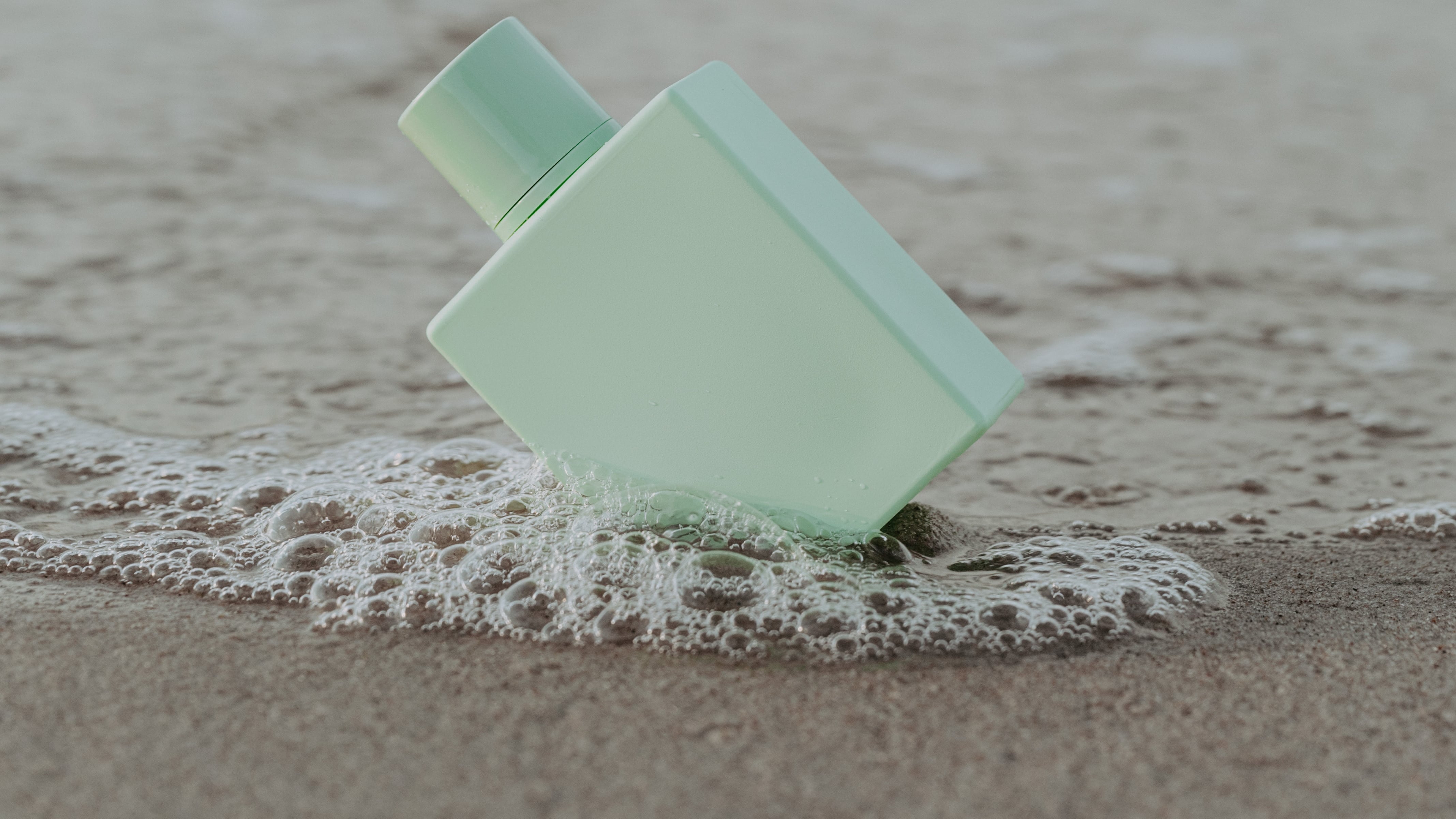 Frasco de perfume na areia do mar sendo acertado por onda
