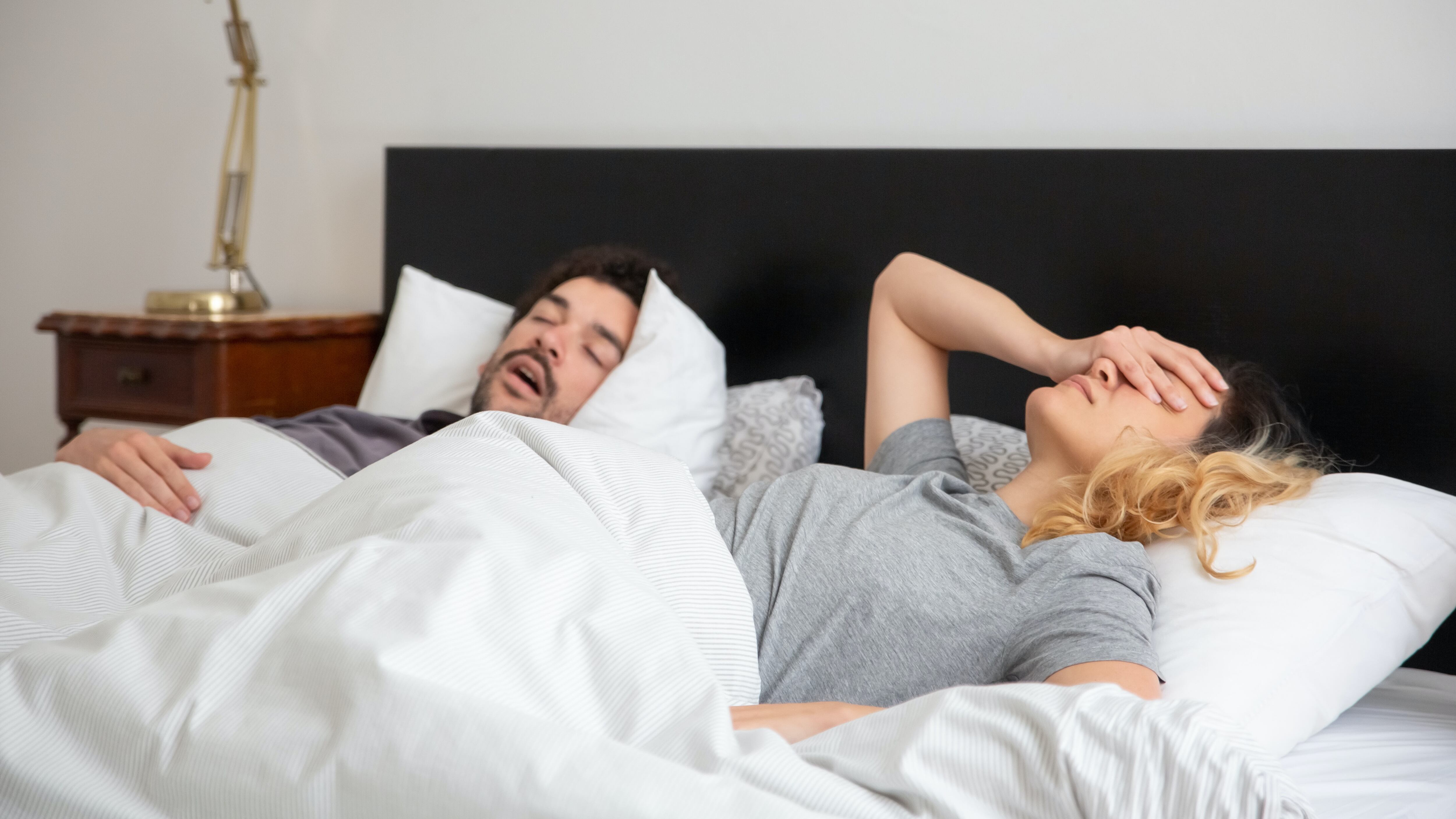 Homem roncando ao lado de mulher na cama, que perdeu o sono