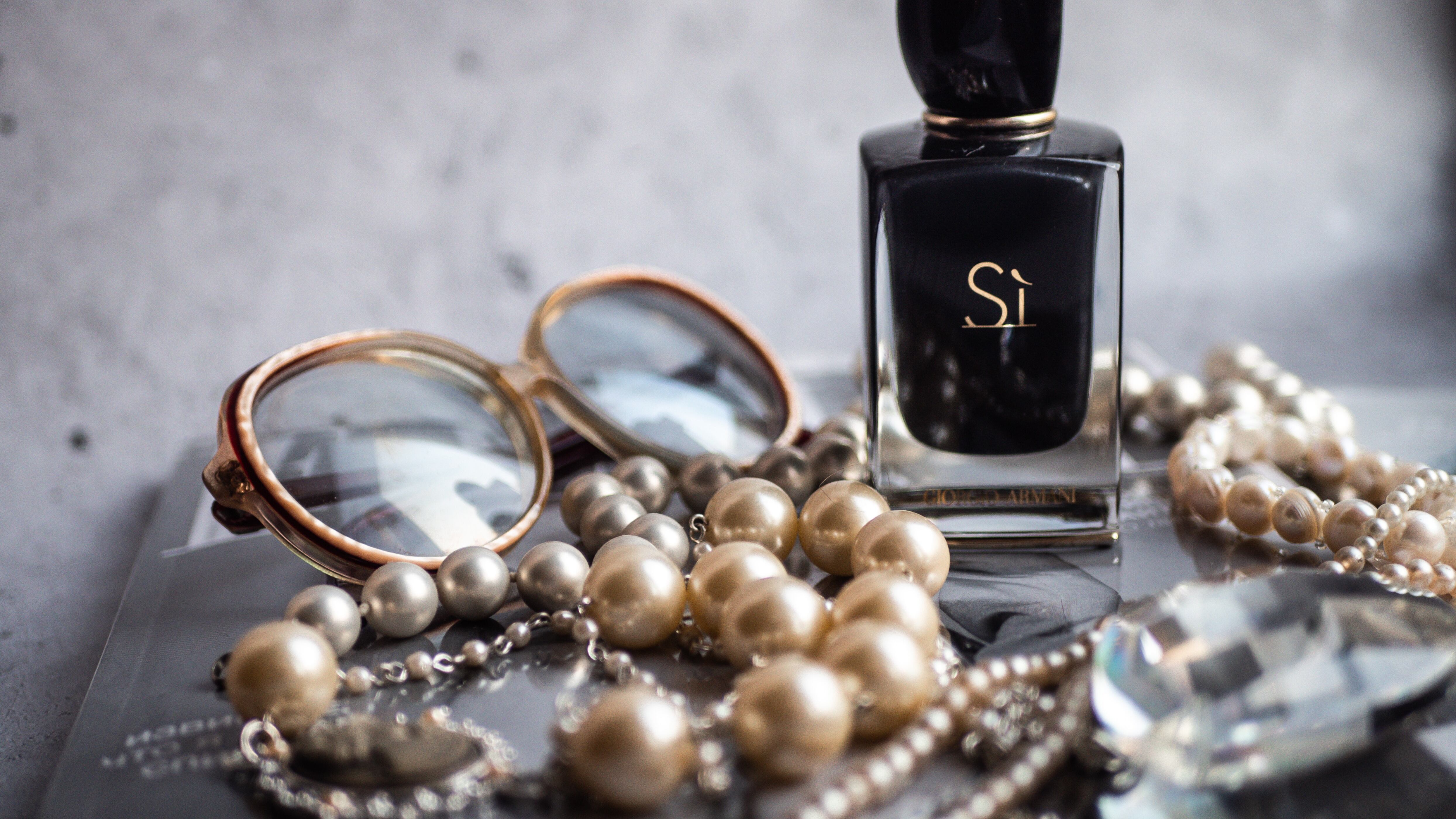 Frasco de perfume Sì ao lado de óculos e colar de pérolas