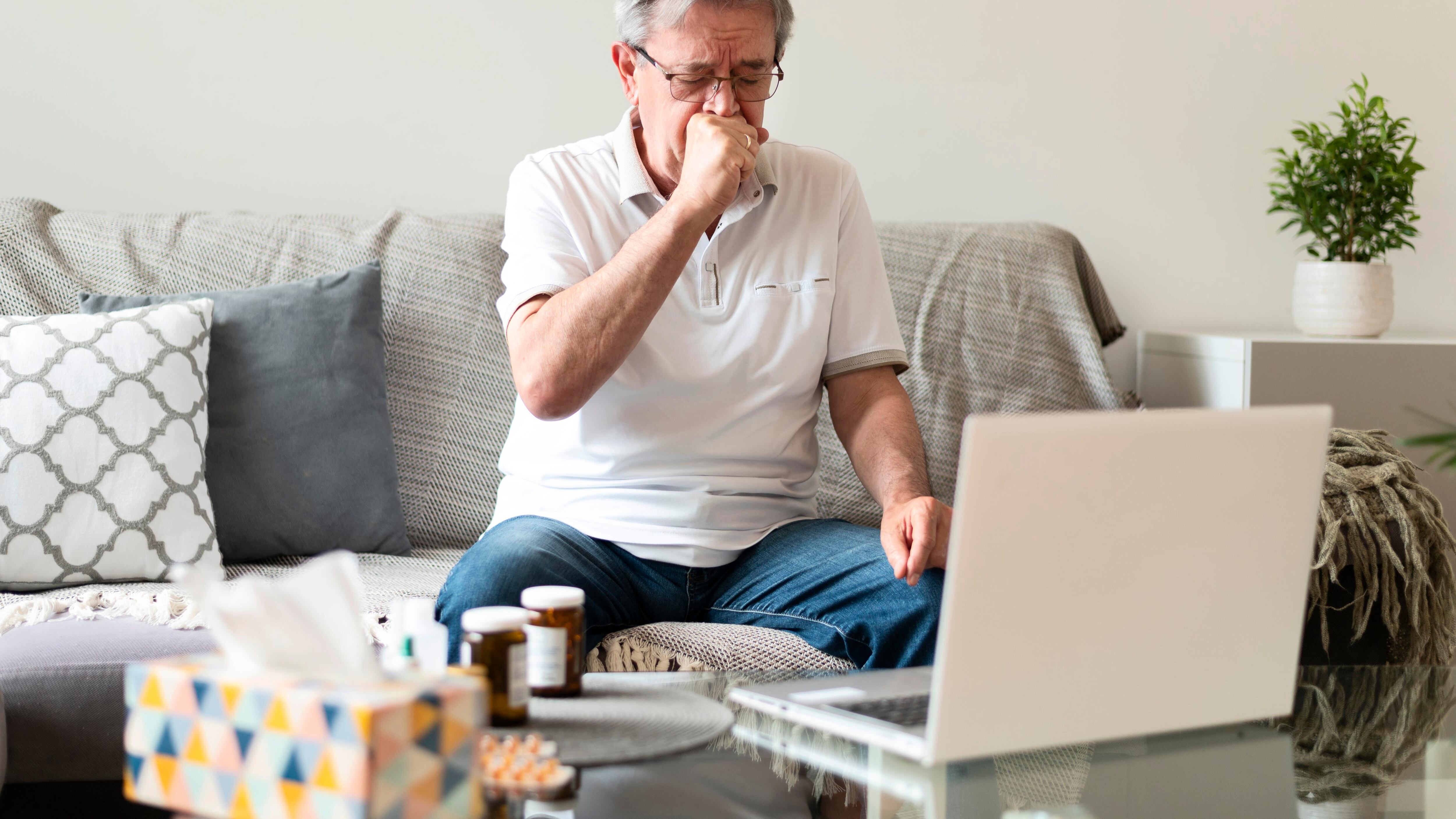 Idoso com computador cobrindo a boca ao tossir