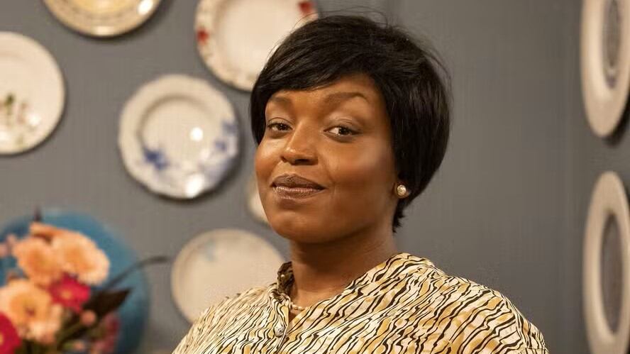 Belize Pombal caracterizada como Consuelo, secretária de Marco Aurélio (Alexandre Nero) na novela Vale Tudo, de 2025