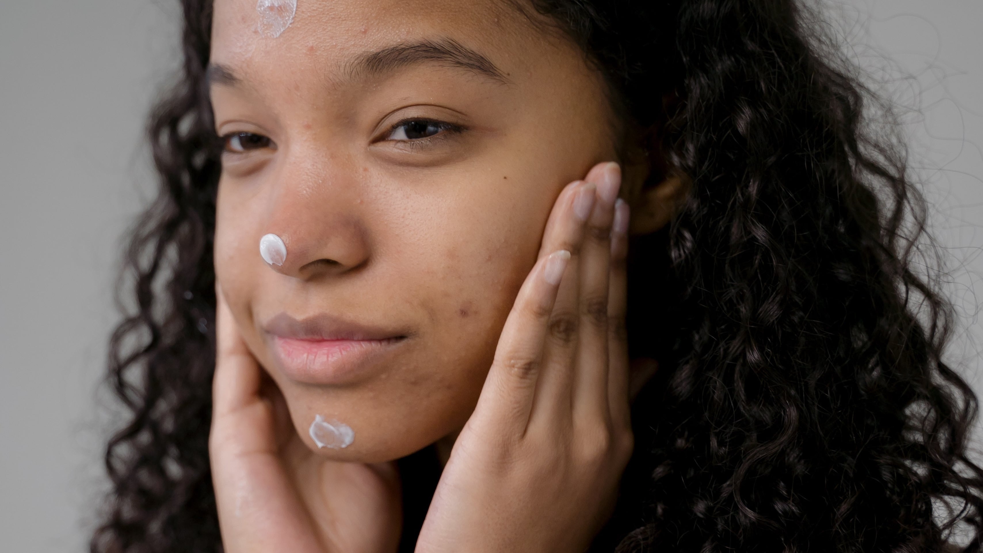 Mulher negra com a mão no rosto e creme espalhado na testa