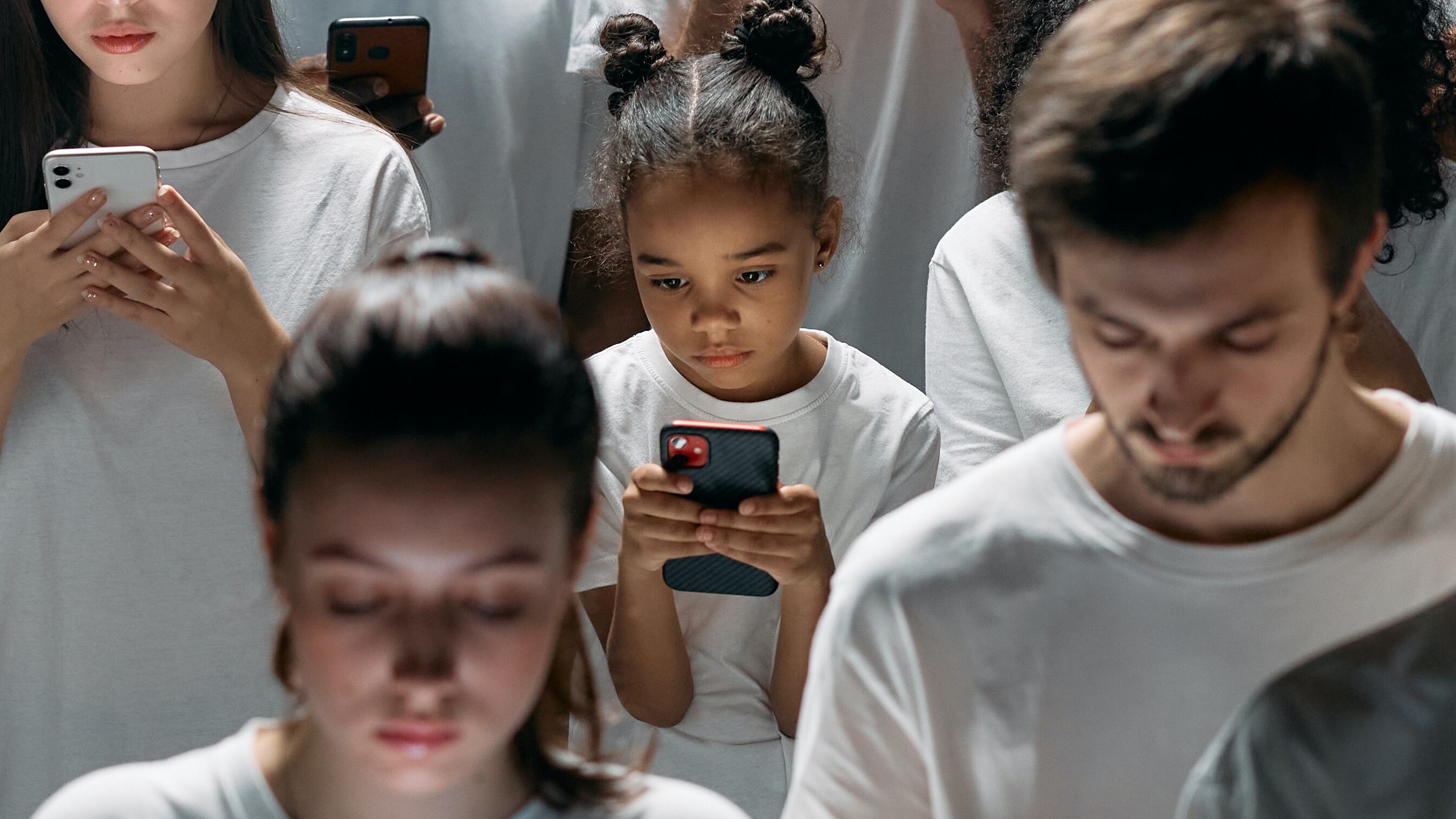 Pessoas com camiseta branca prestando atenção nos celulares