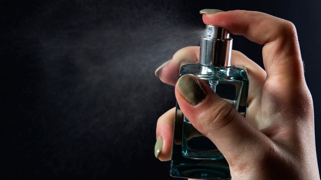 Mão feminina com unhas pintadas de verde borrifando frasco de perfume