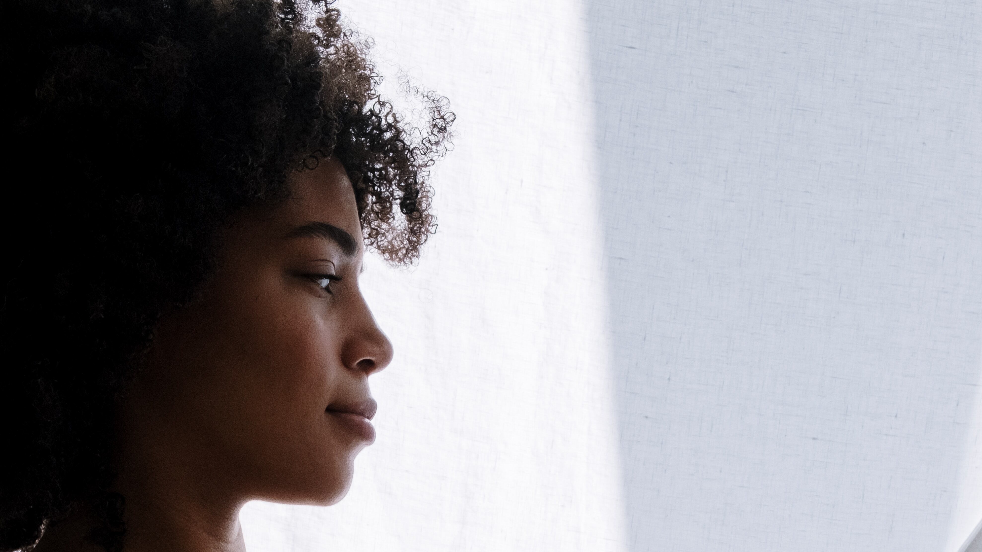 Mulher negra com cabelo cacheado grávida olhando pela janela