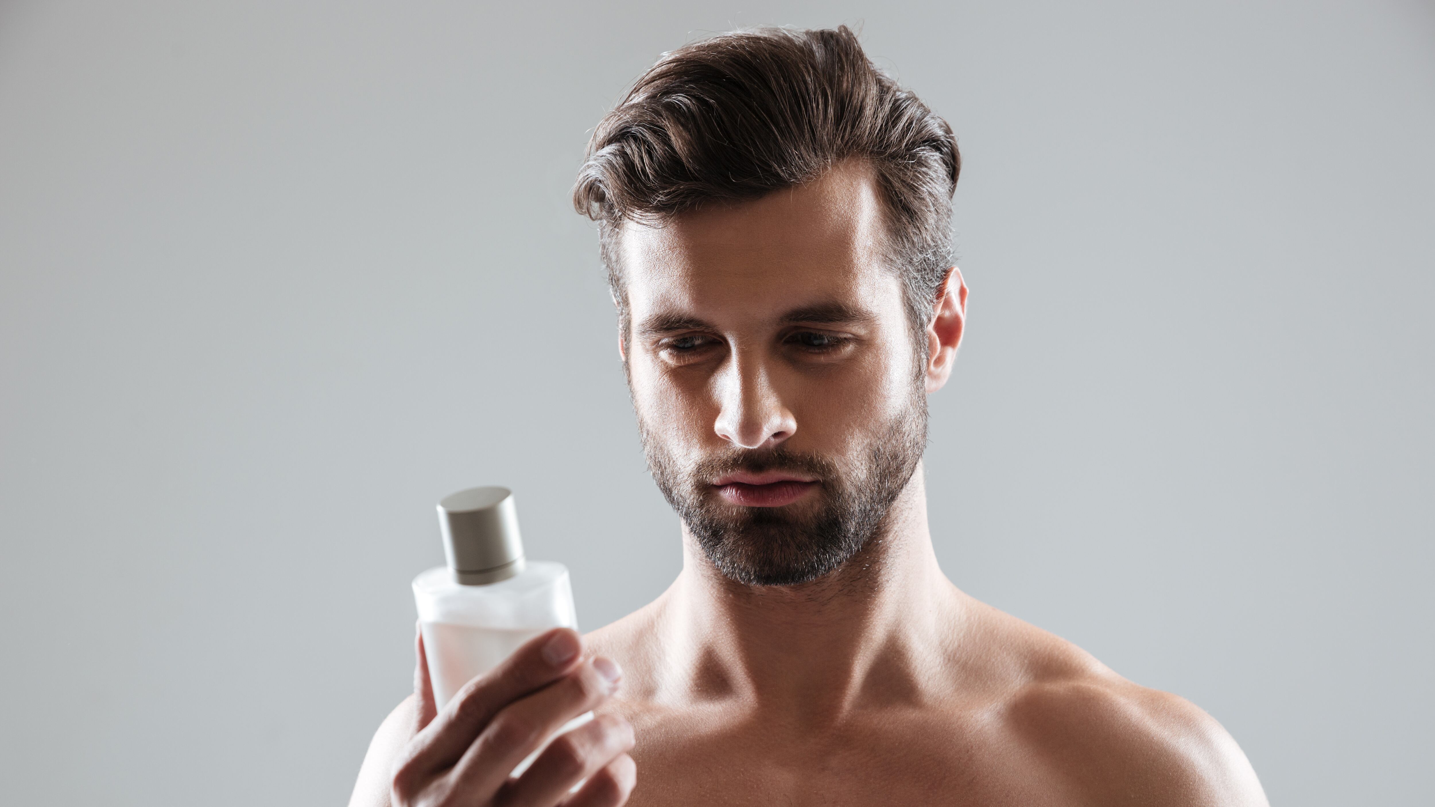 Homem sem camisa olhando para frasco de perfume