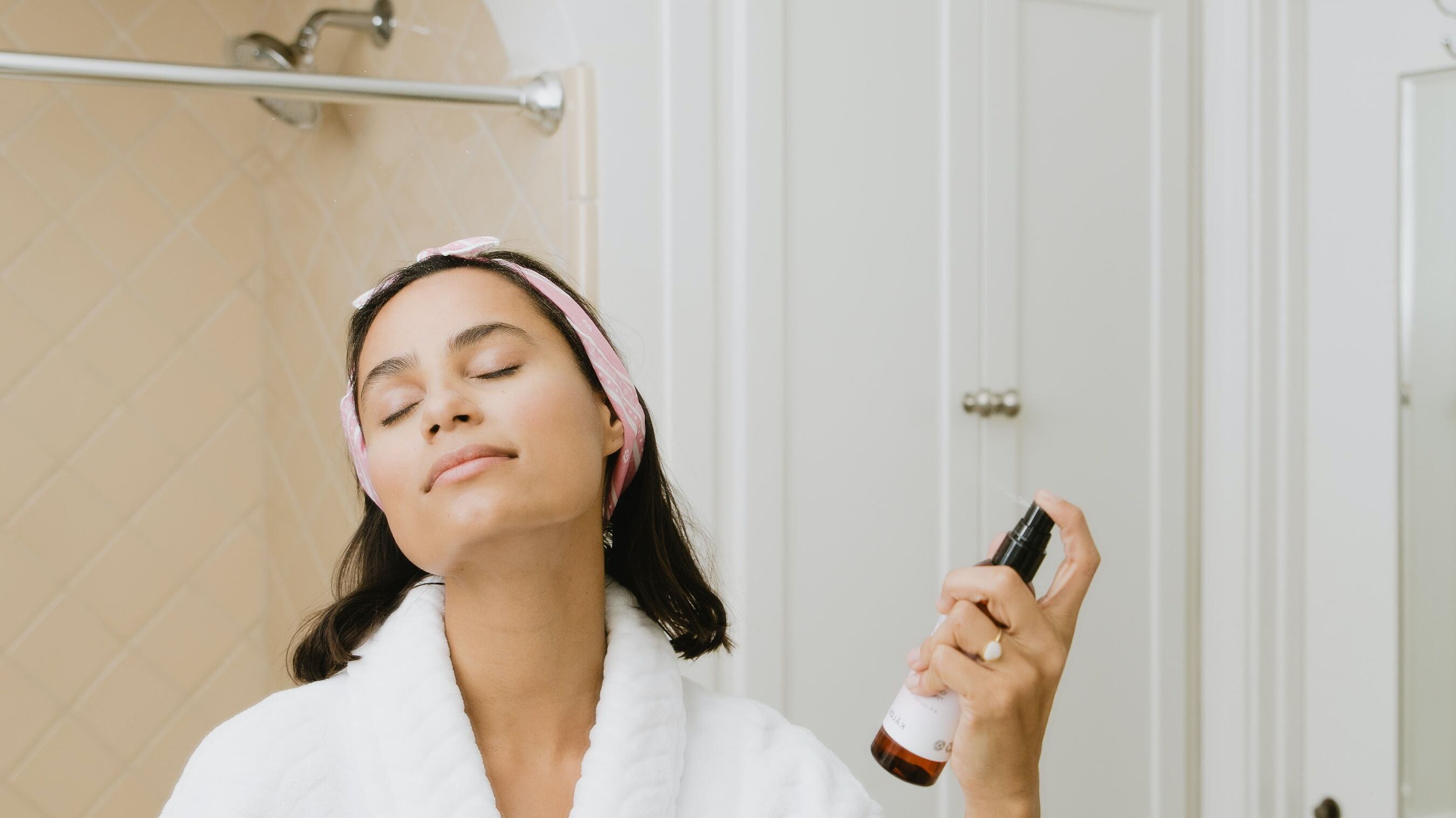 Mulher de roupão no banheiro espirrando spray no pescoço