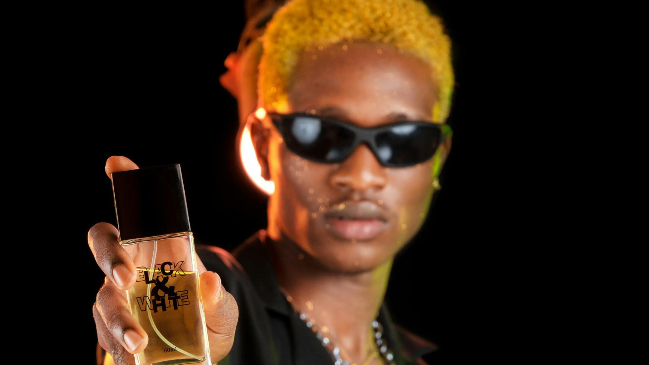 Homem negro loiro de óculos escuros segurando perfume