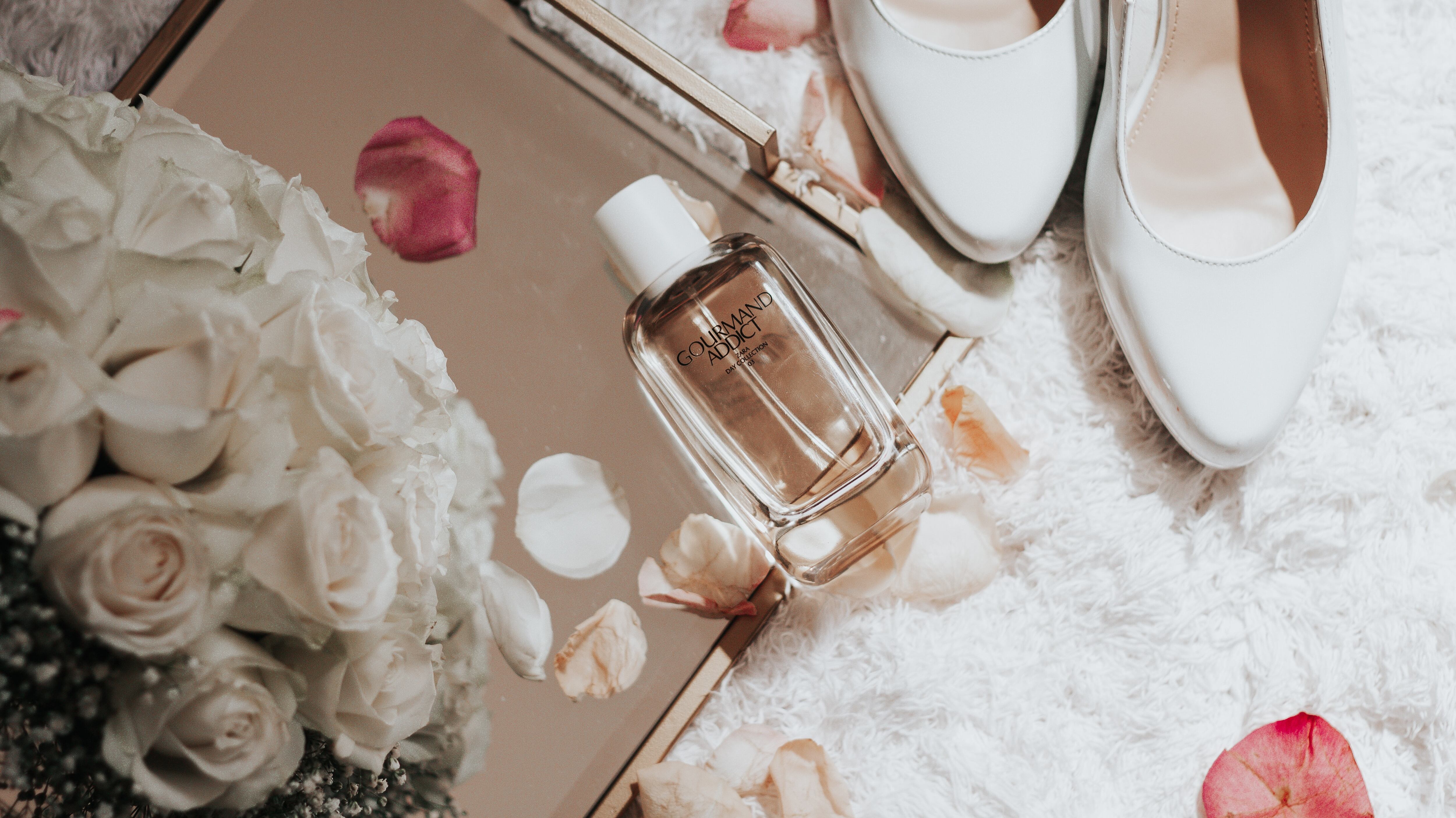 Frasco de perfume ao lado de sapato branco e flores brancas