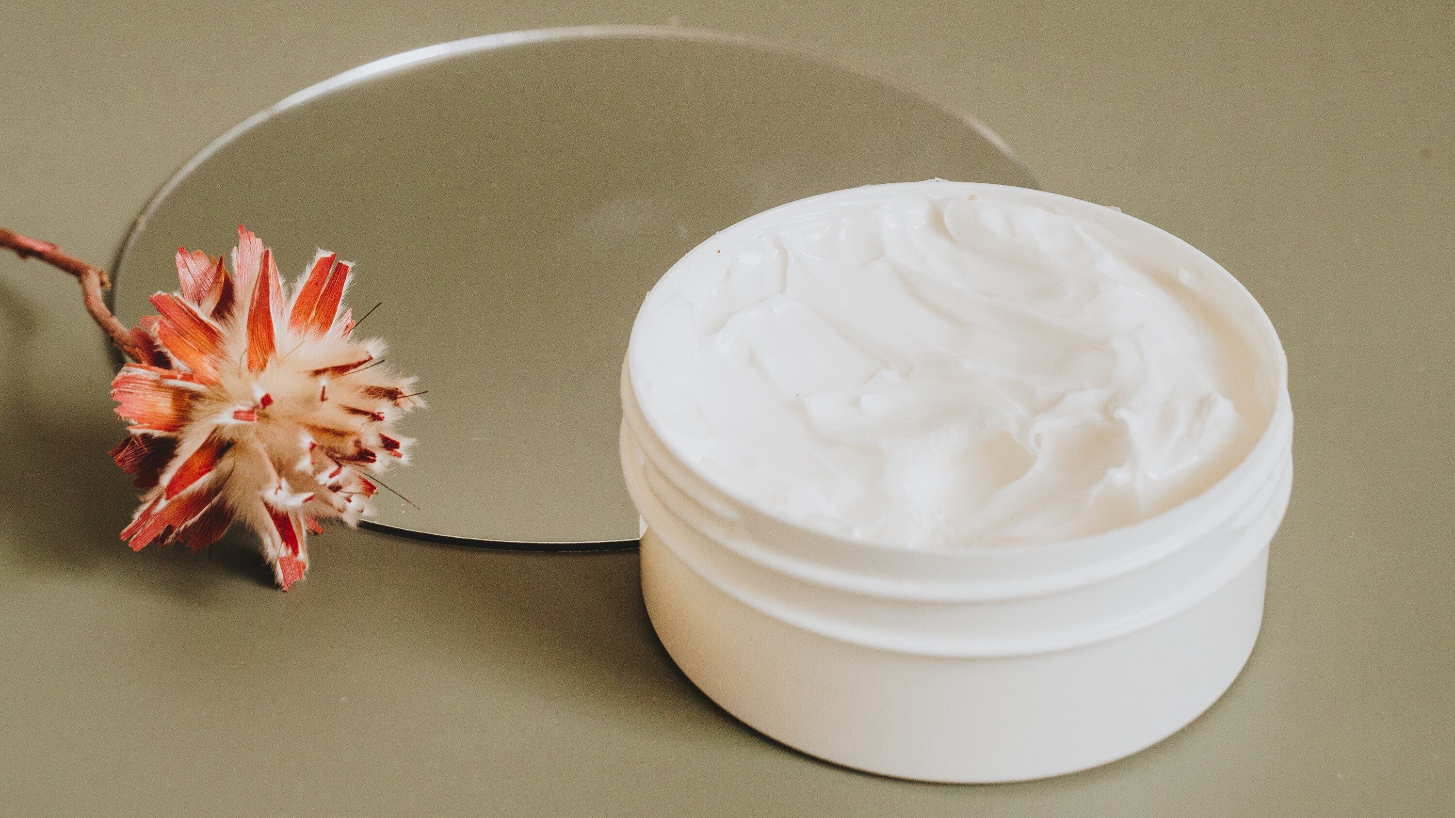 Pote de creme ao lado de espelho e flor