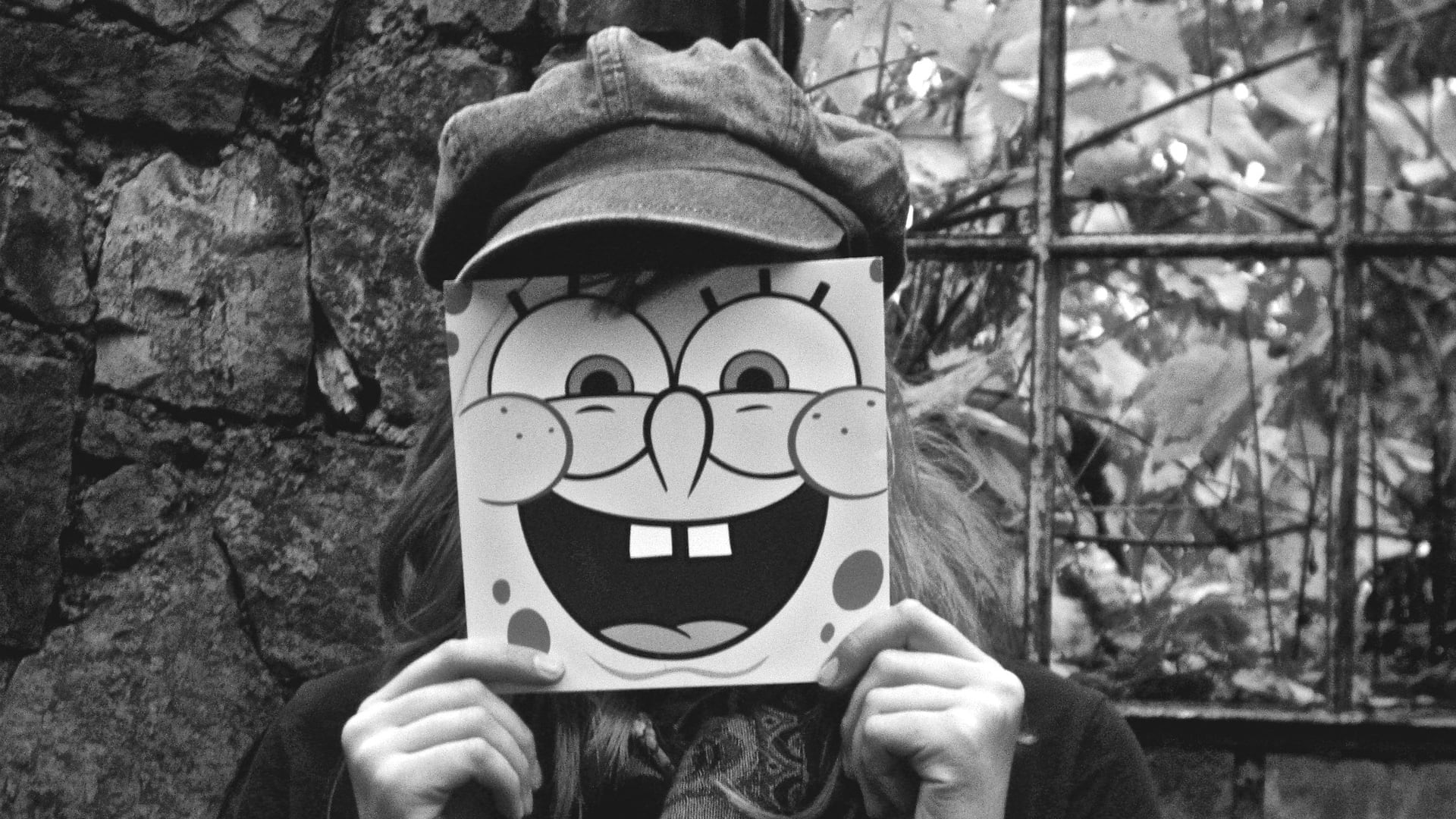Imagem em preto e branco de pessoa com chapéu e máscara do Bob Esponja
