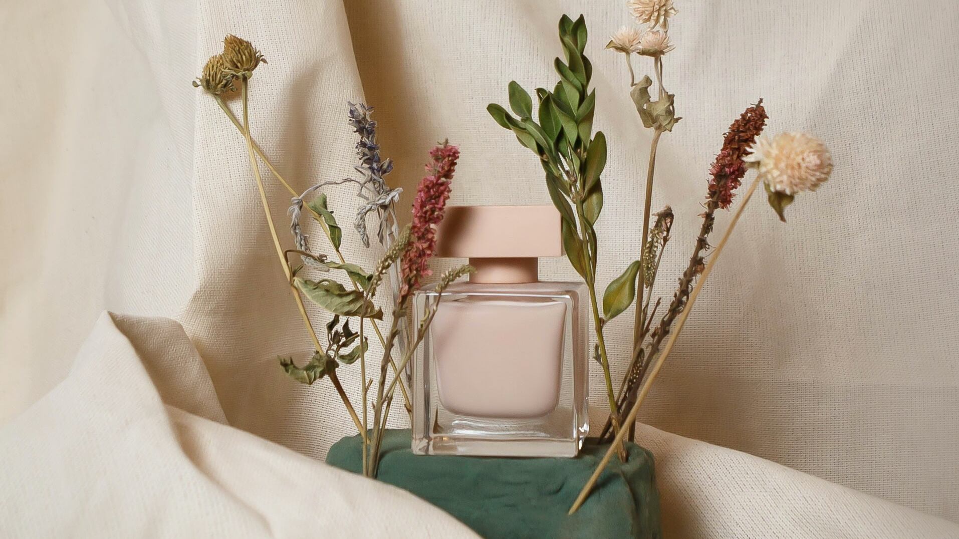 Frasco de perfumes rosa ao lado de flores secas