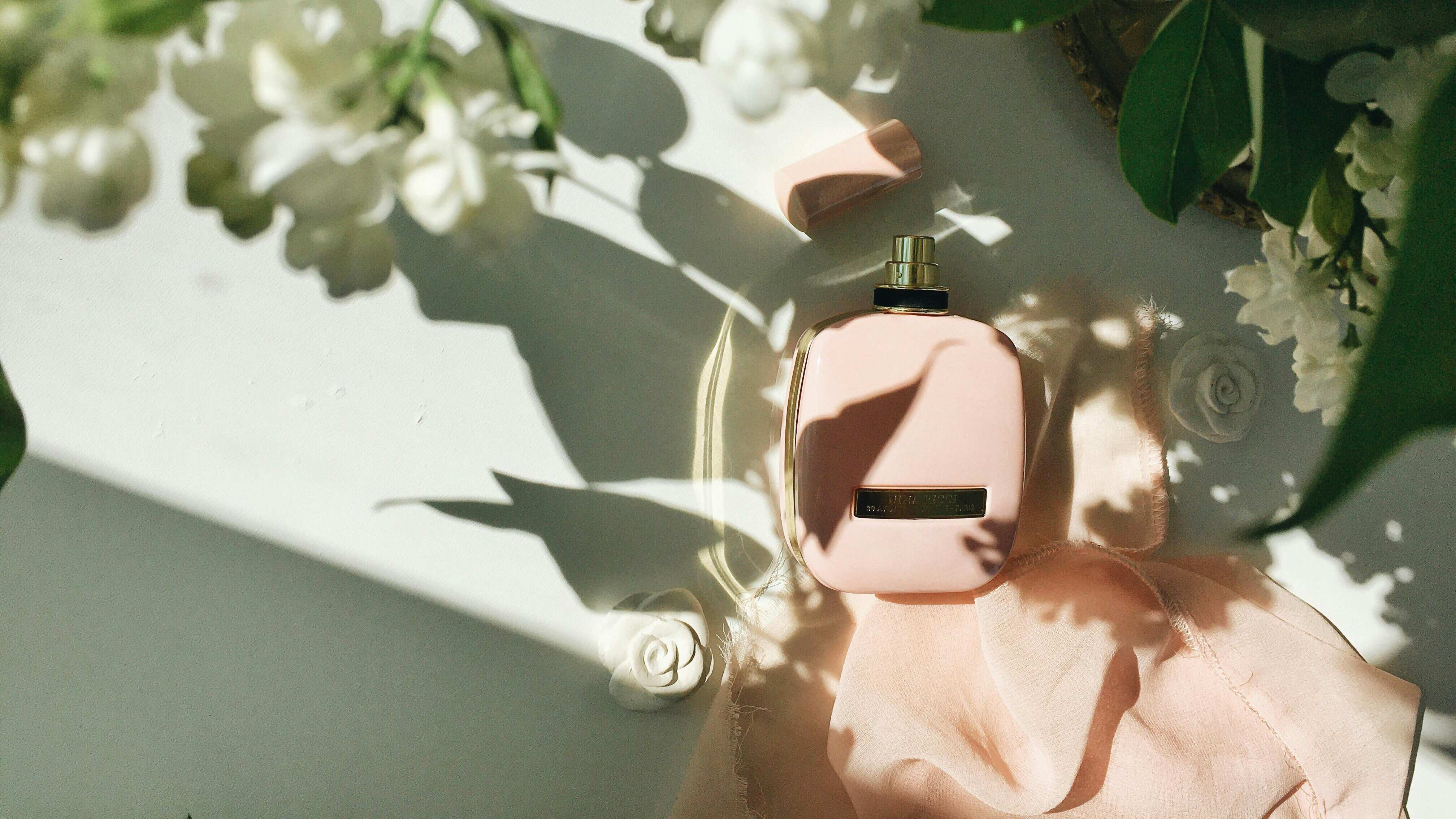Frasco de perfume rosa ao lado de flores brancas