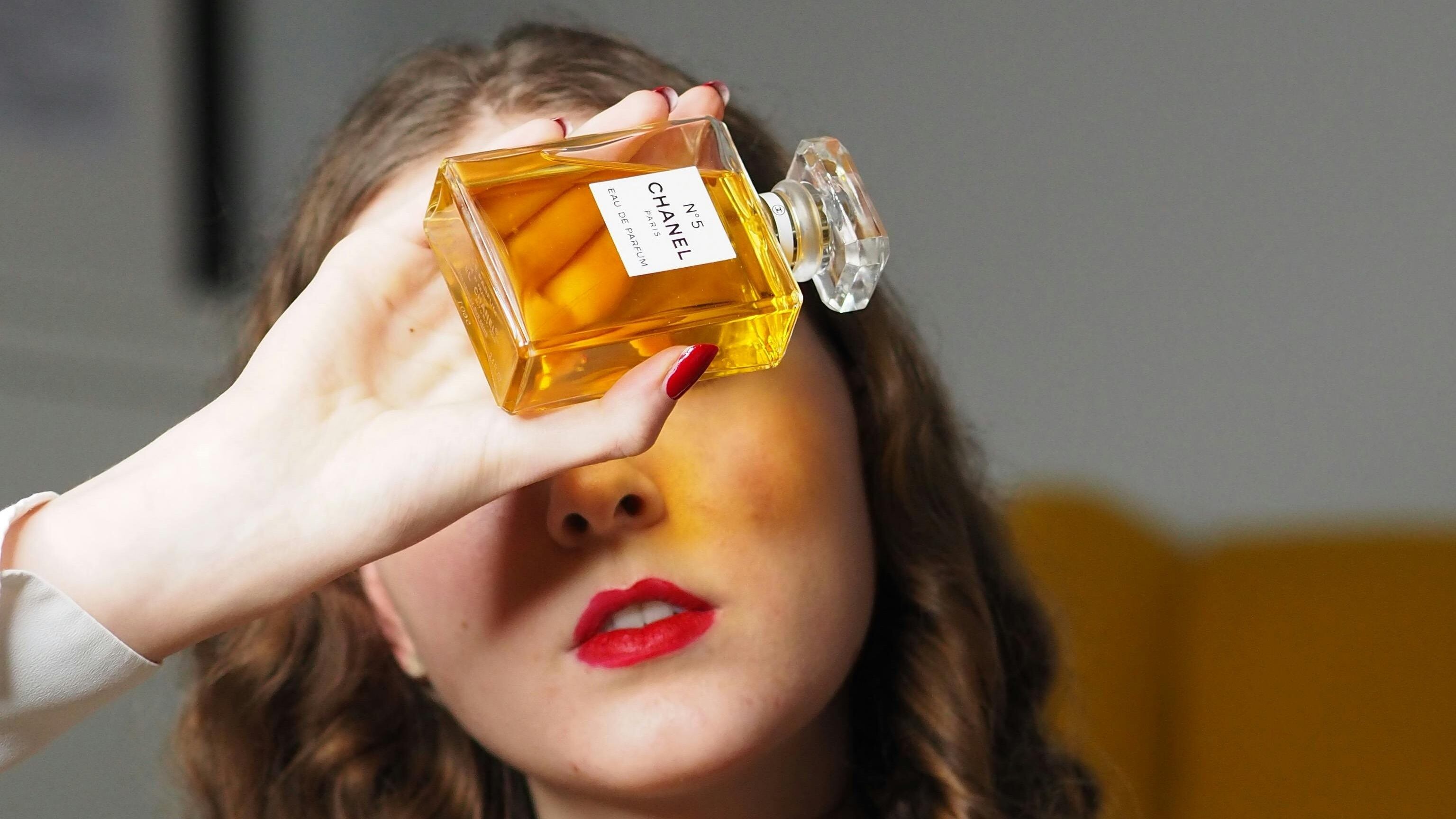 Mulher branca e ruiva segurando frasco de perfume Chanel Nº5