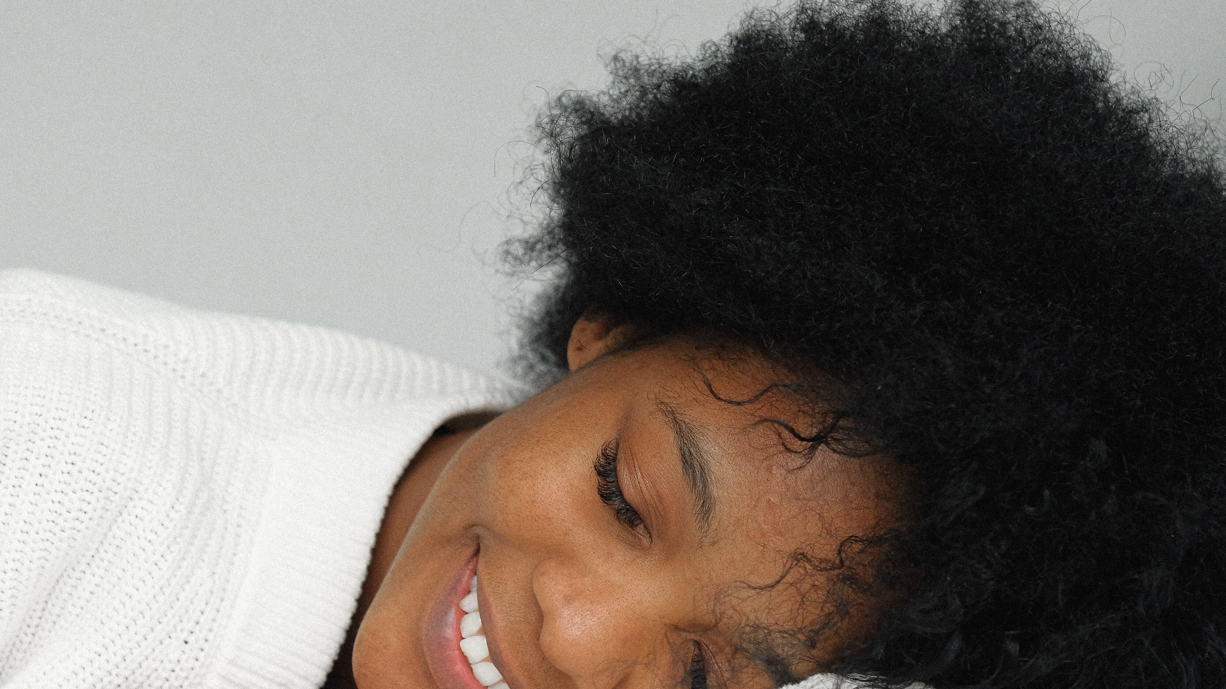 Mulher negra deitada com olho fechado sorrindo