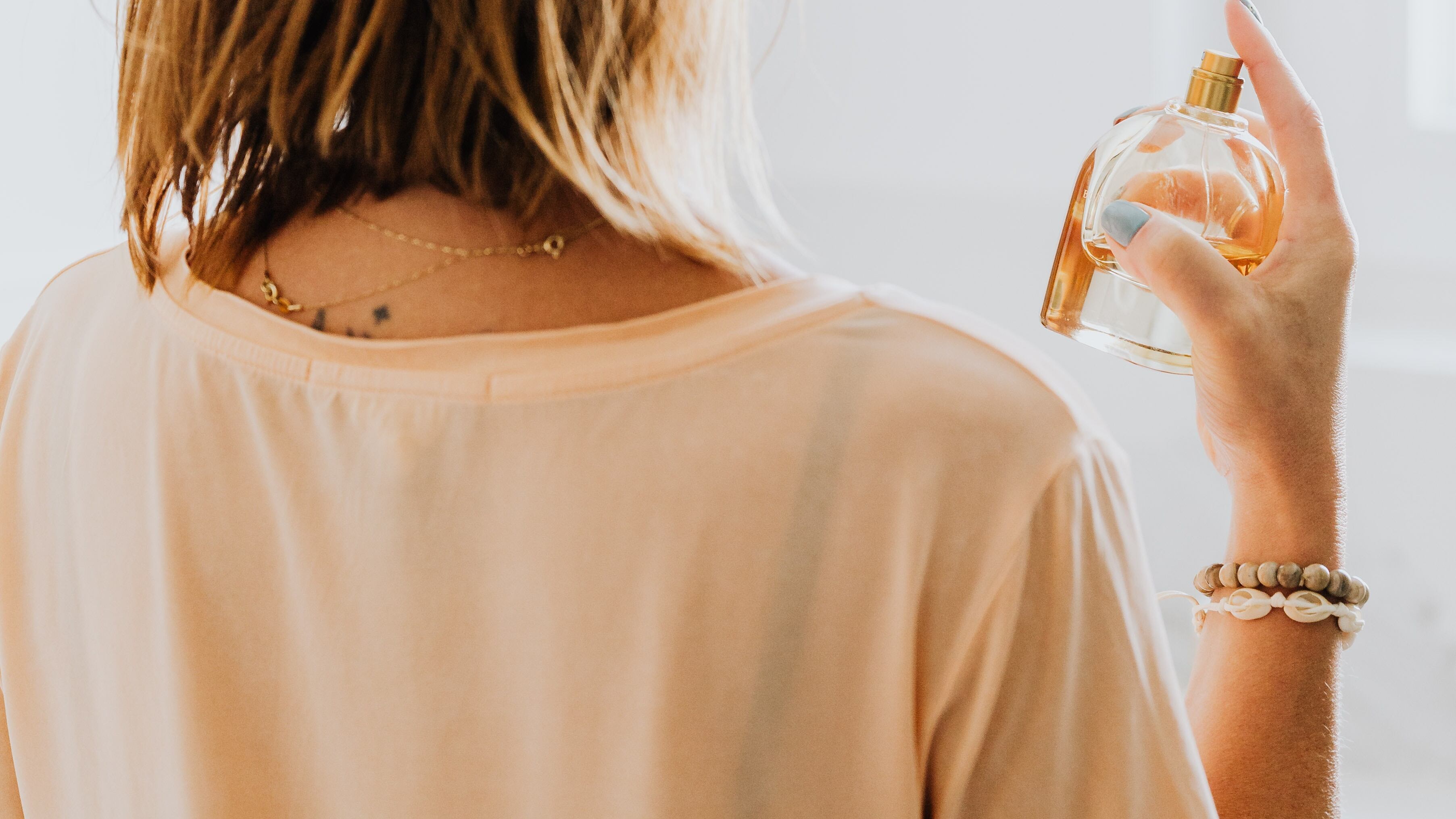 Mulher loira de costas espirrando perfume no pescoço