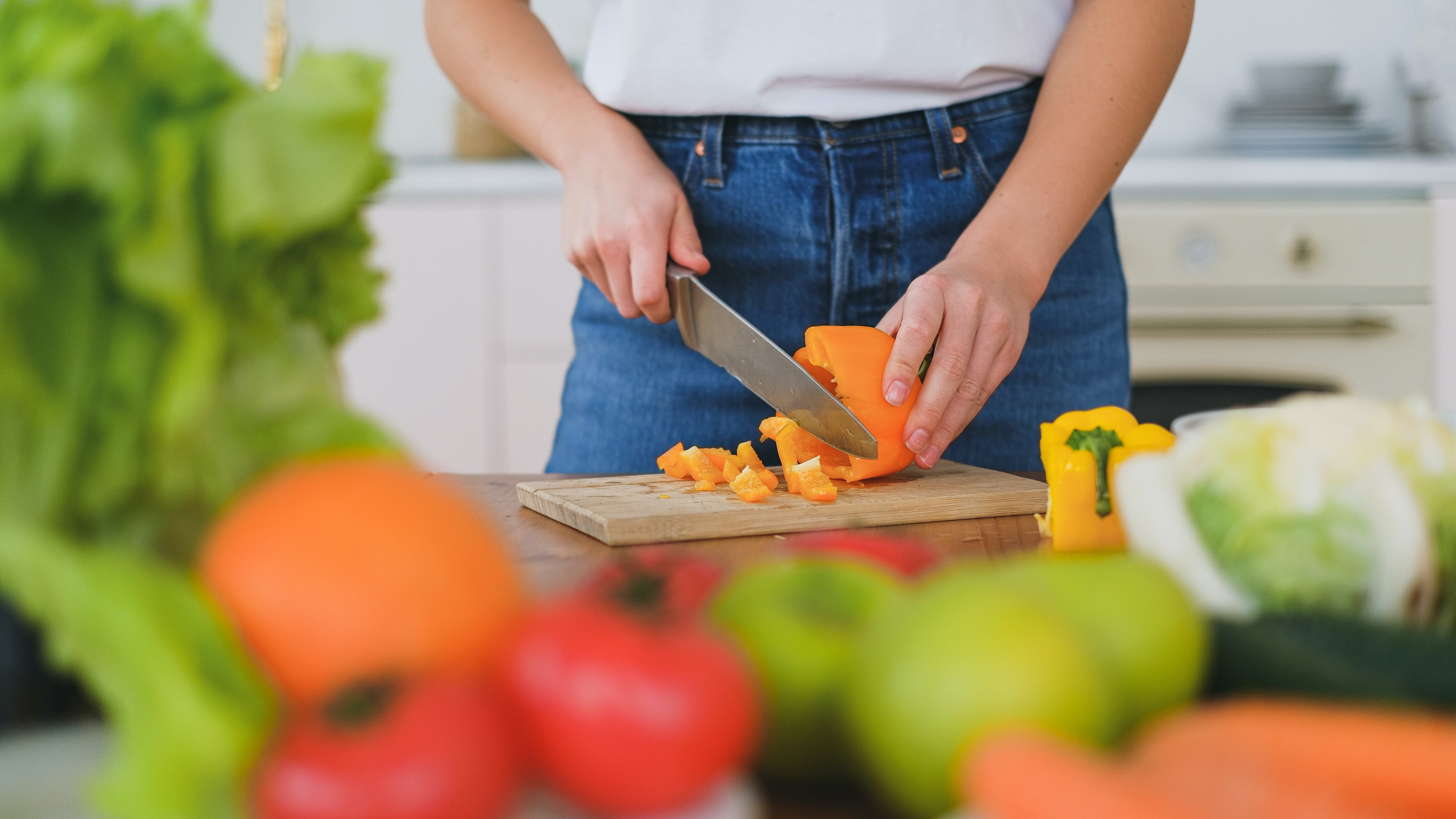 Mulher cortando legumes ao lado de diversos alimentos saudáveis.