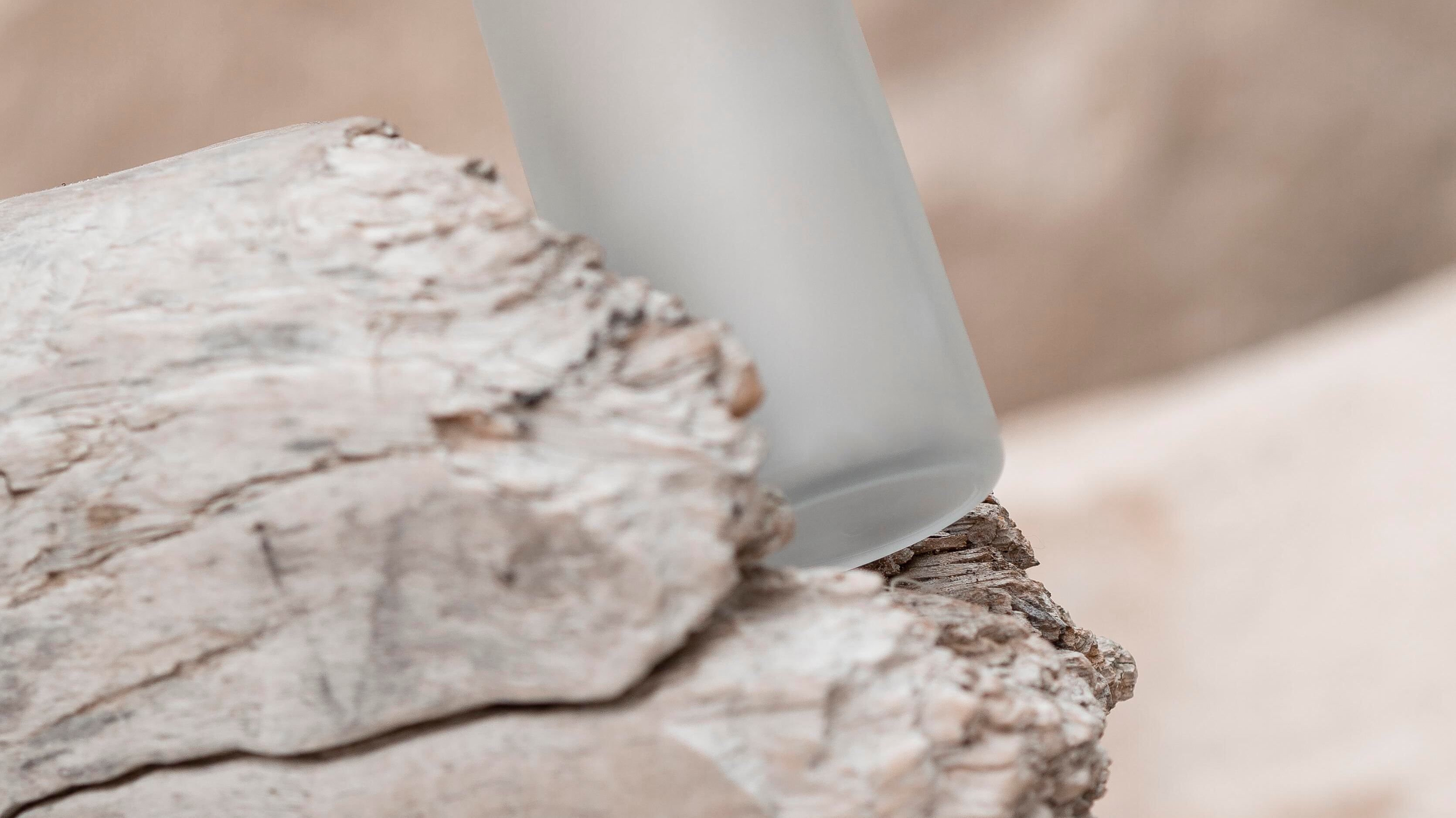 Frasco de perfume transparente com tampa prateada em cima de uma pedra