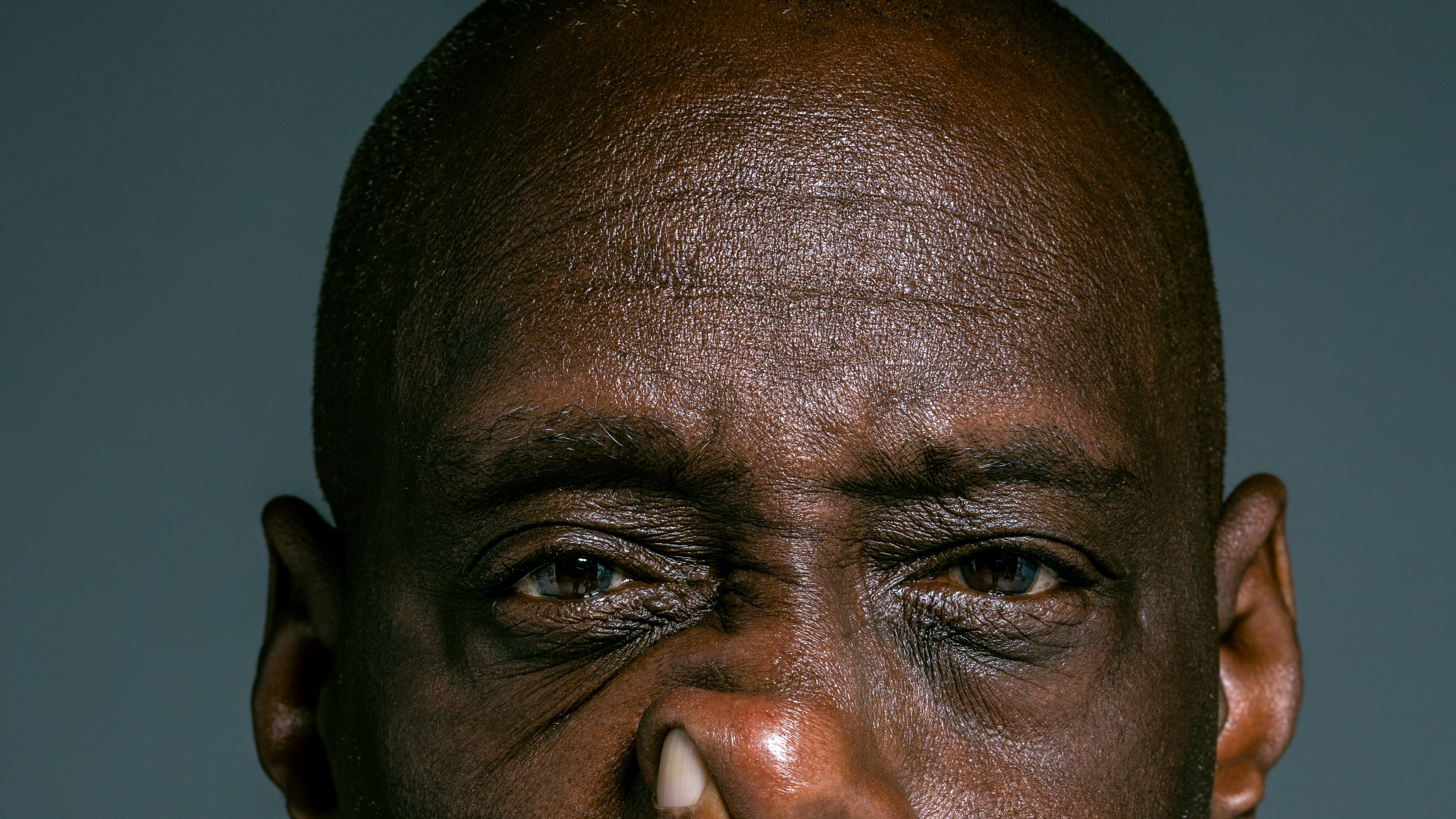 Homem preto careca de camiseta preta colocando dedo indicados no nariz