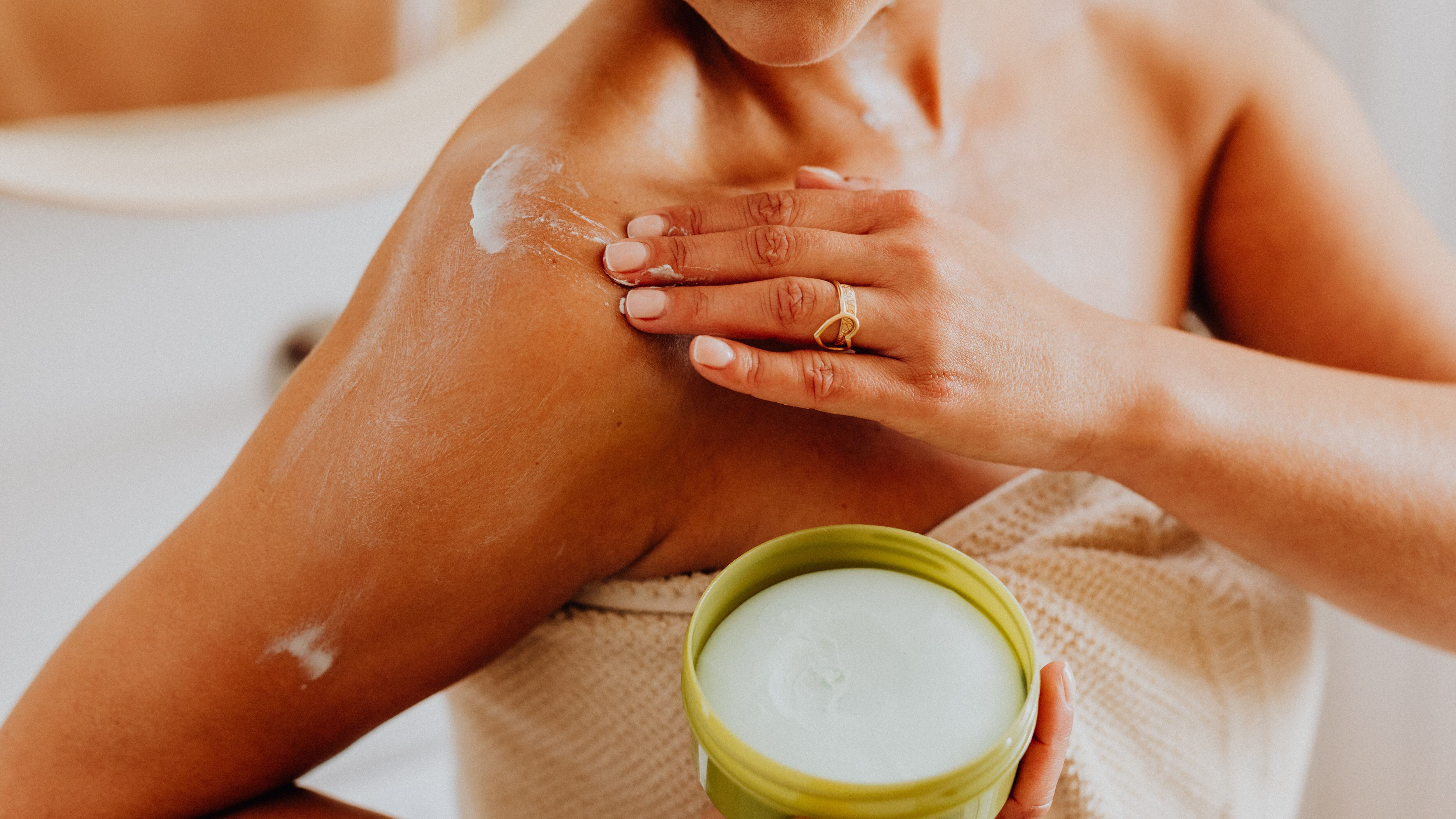 Silhueta feminina de toalha passando creme no braço