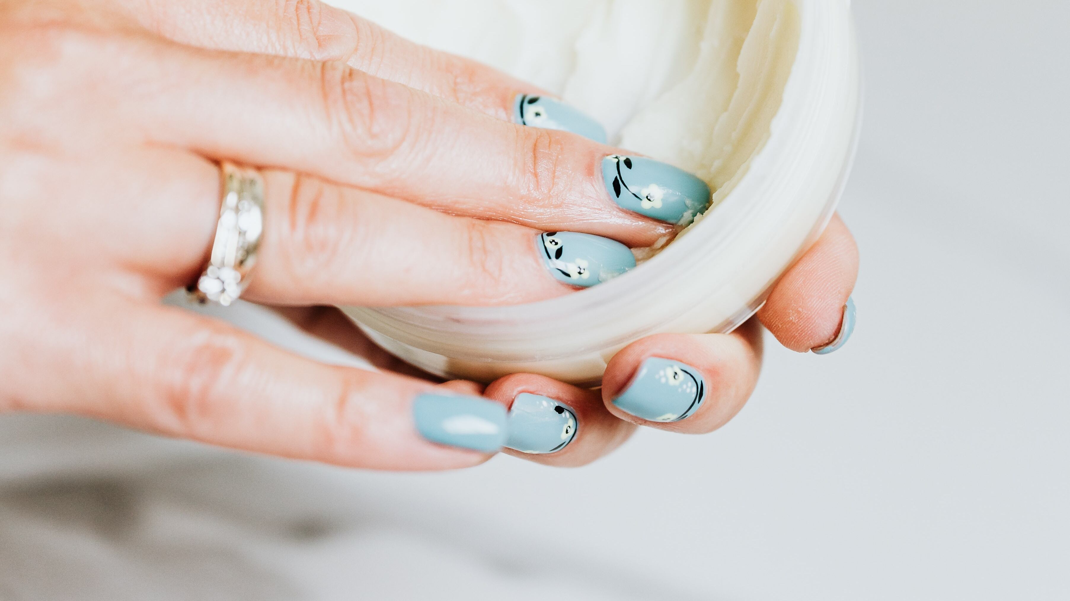 Mão feminina com unhas pintadas dentro de pote de hidratante