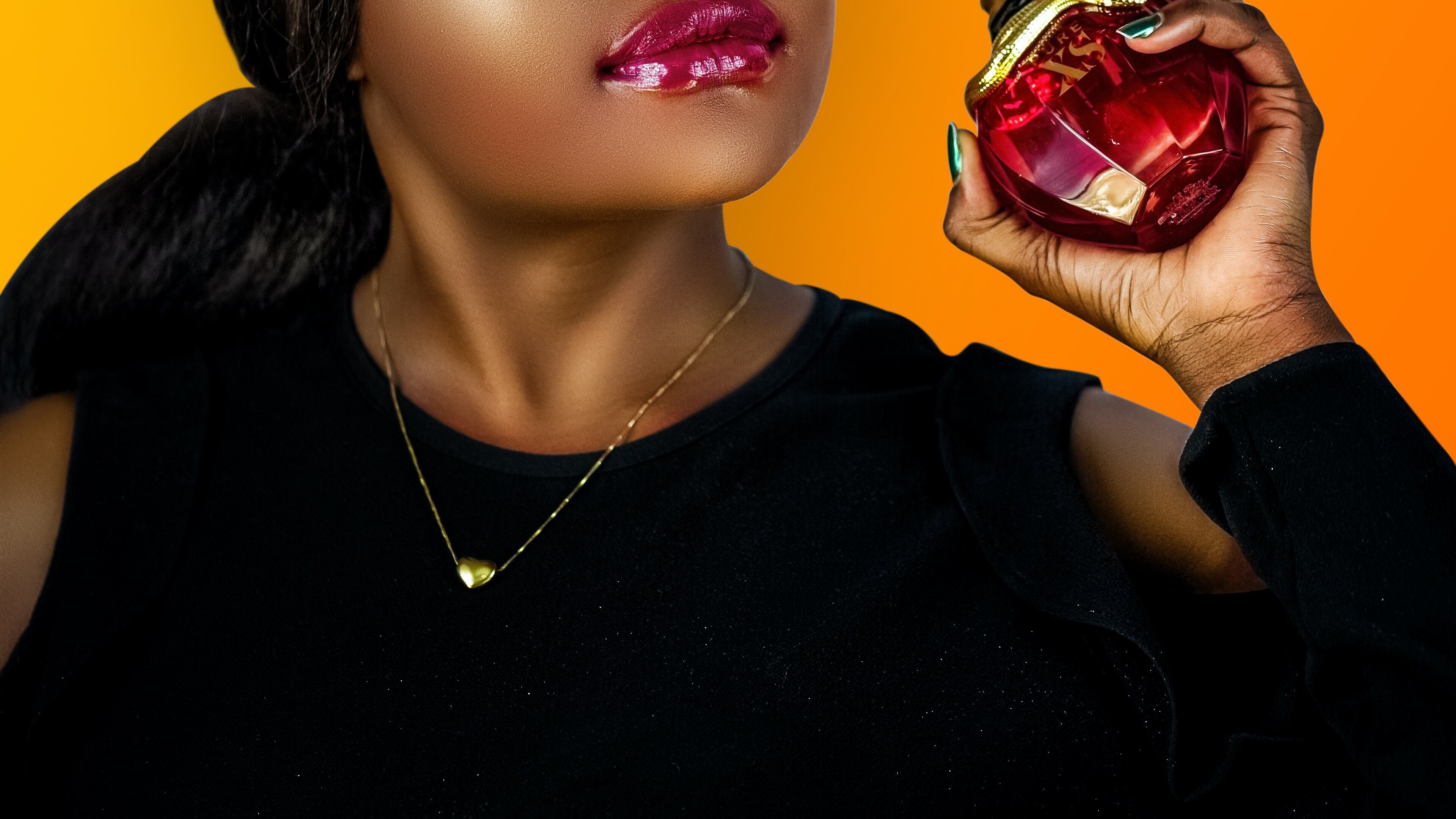 Mulher negra segurando frasco de perfume vermelho