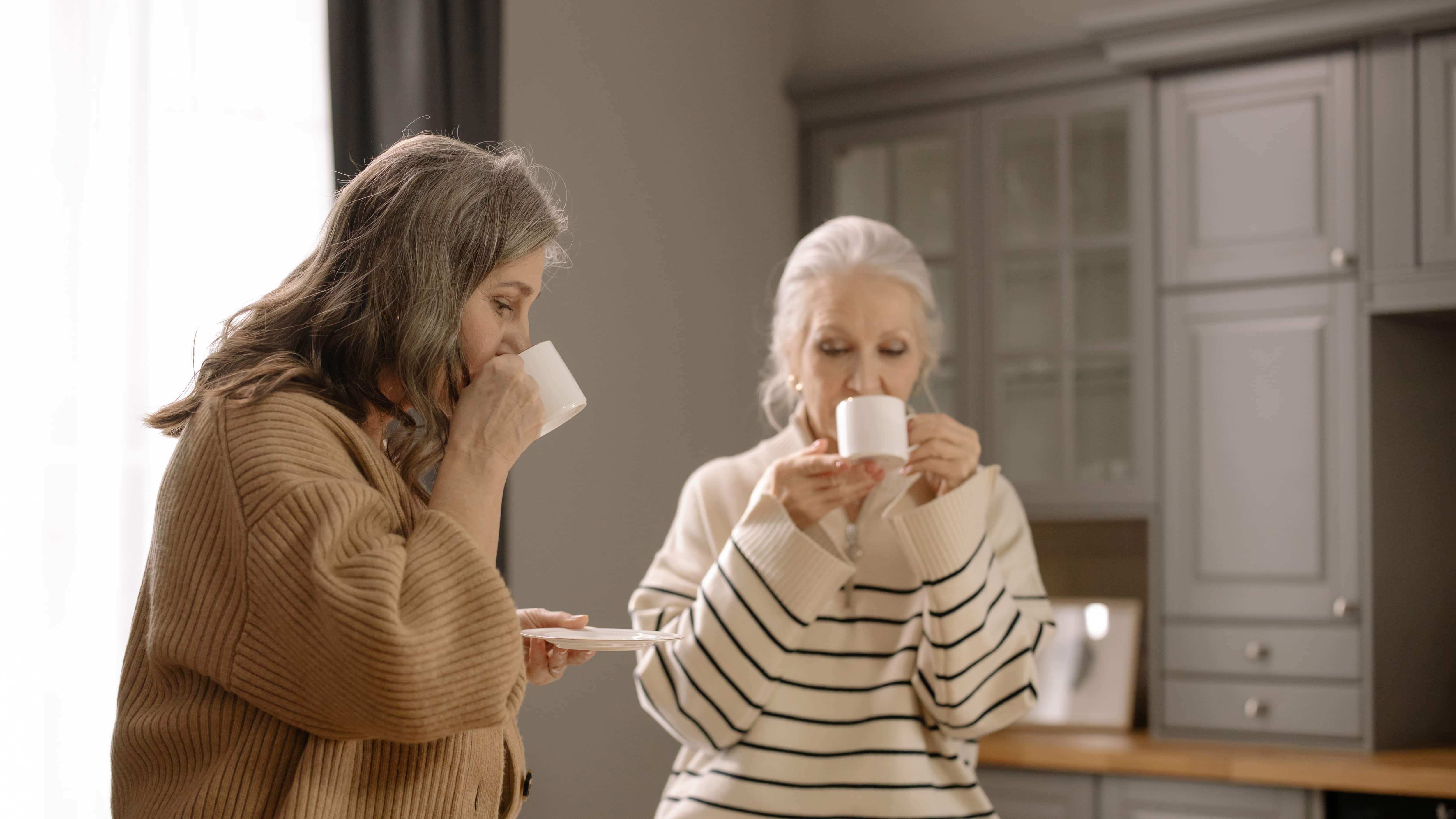 Duas senhoras brancas de cabelos grisalhos sentadas tomando chá em xícaras brancas