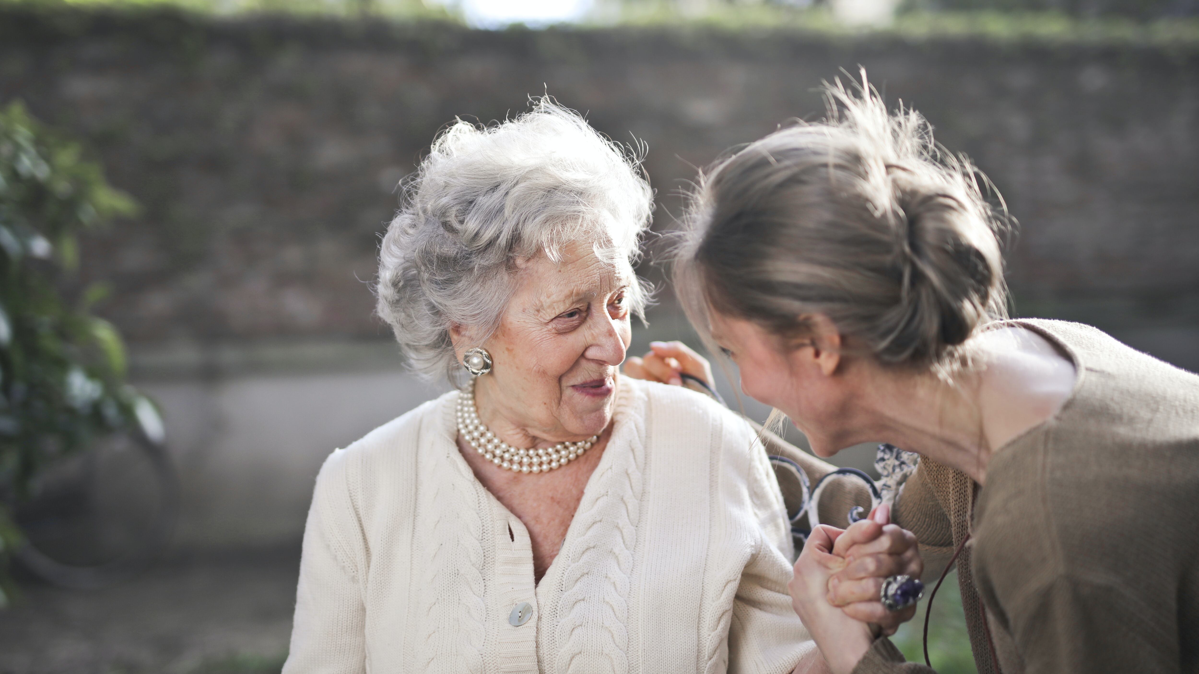 Senhora com brinco e colar de pérolas conversando com mulher