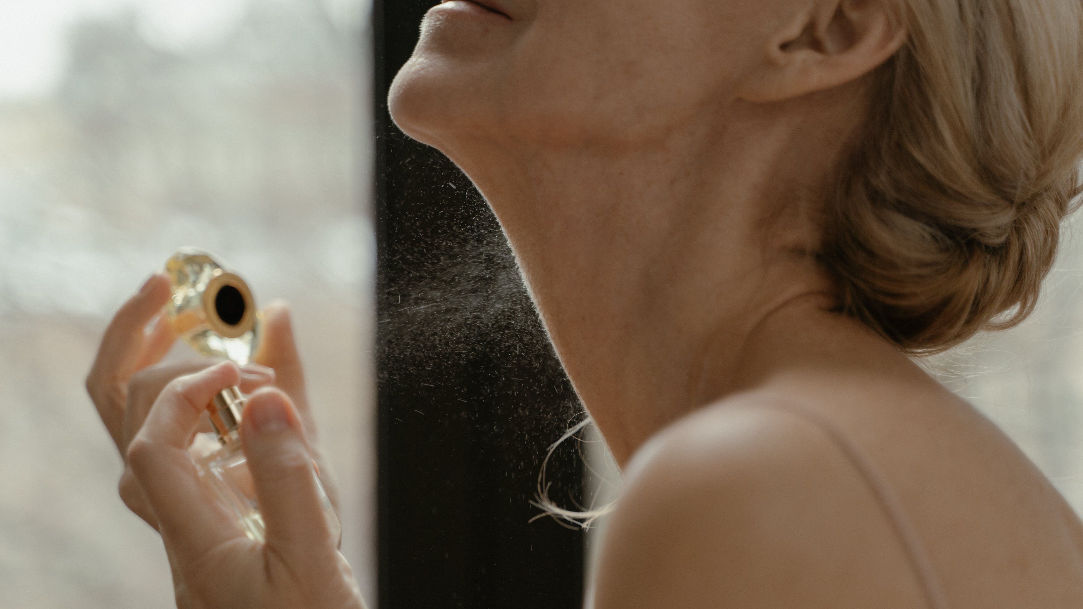 Mulher branca e loira borrifando perfume no pescoço