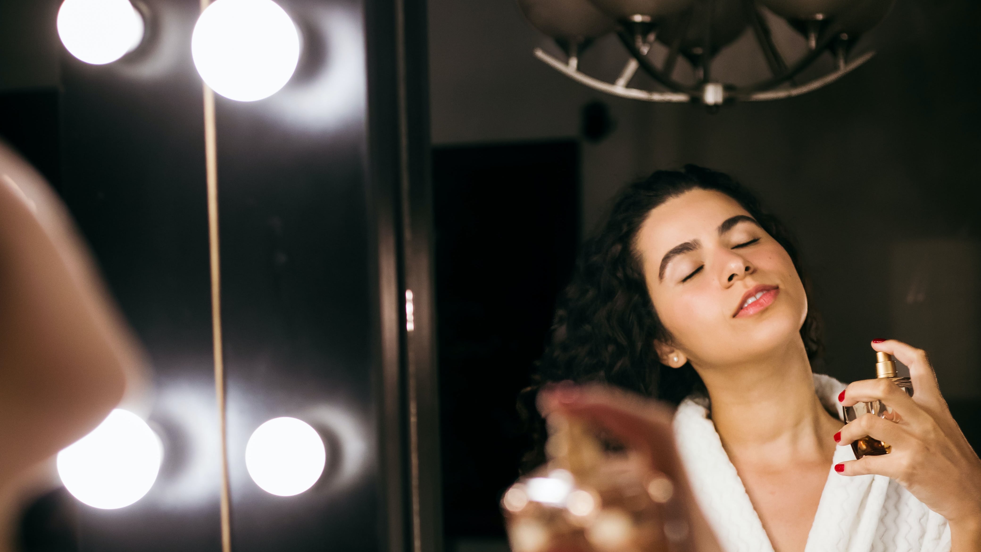 Mulher de roupão borrifando perfume em frente ao espelho