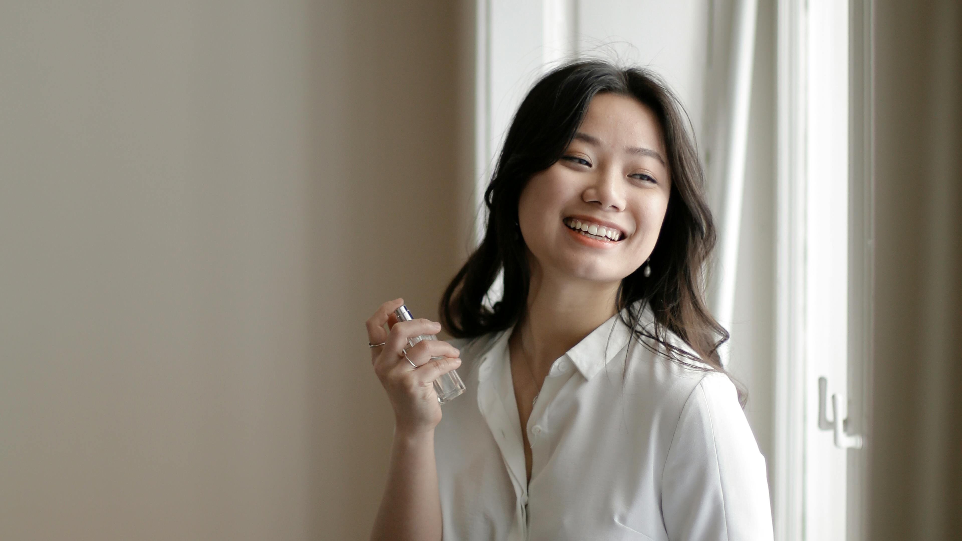 Mulher asiática sorrindo borrifando perfume no pescoço