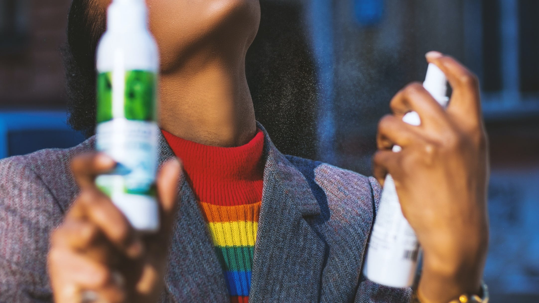 Mulher negra segurando body splash com uma mão e espirrando com outra